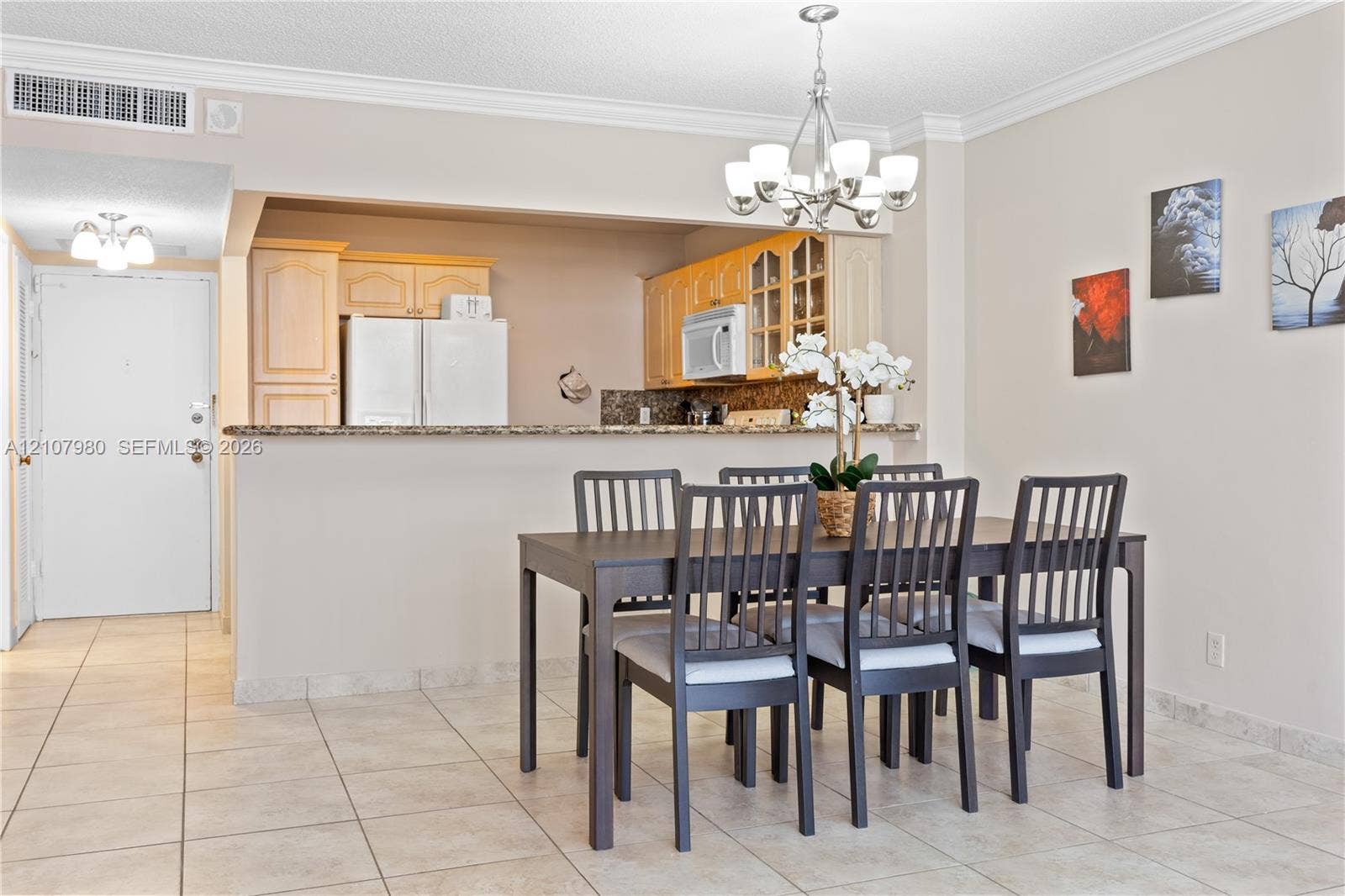 3725 S Ocean Drive, #1120, Hollywood, Hollywood, FL 33019 Dining area featuring ceramic tile flooring, crown molding, and a multi-light chandelier, complemented by a kitchen with built-in cabinetry and a stone-topped breakfast bar