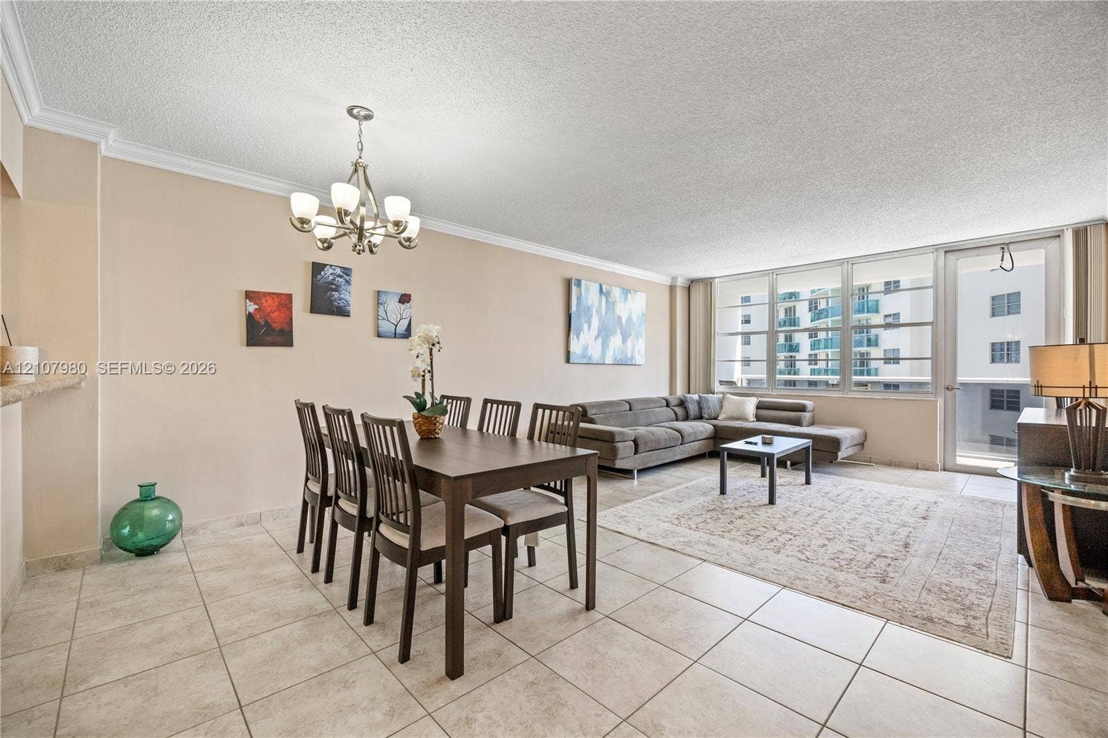 3725 S Ocean Drive, #1120, Hollywood, Hollywood, FL 33019 Open-concept living and dining area featuring large-format tile flooring, crown molding, multi-light chandelier, and floor-to-ceiling windows with a glass-paneled door