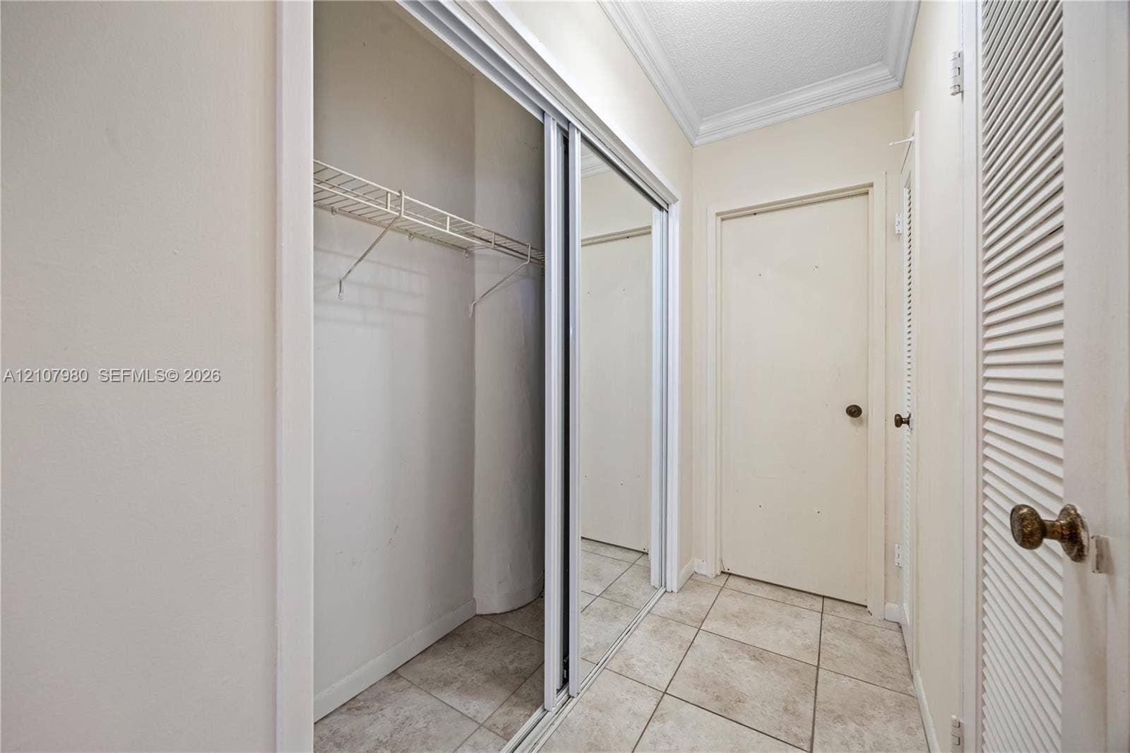3725 S Ocean Drive, #1120, Hollywood, Hollywood, FL 33019 Closet featuring mirrored sliding doors, integrated wire shelving, crown molding, and tiled flooring
