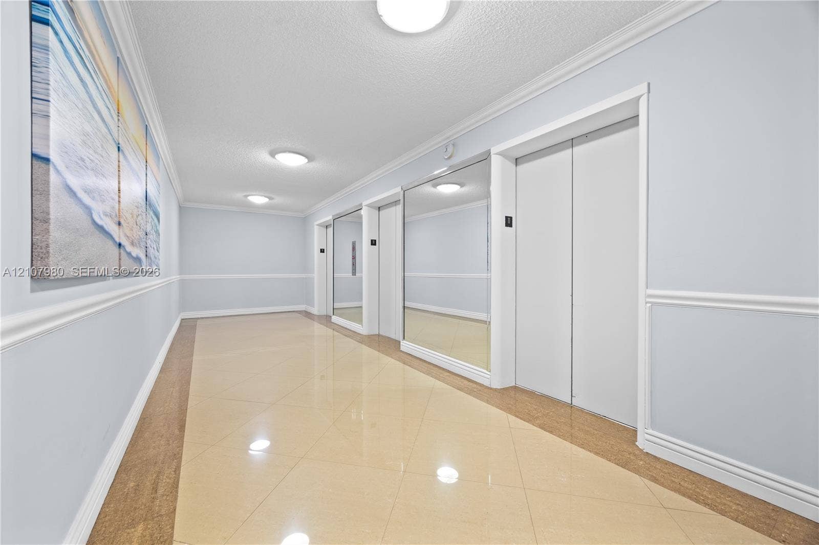 3725 S Ocean Drive, #1120, Hollywood, Hollywood, FL 33019 Common hallway featuring polished tile flooring, wall-mounted mirrors, crown molding, chair rail trim, and flush-mount ceiling lighting