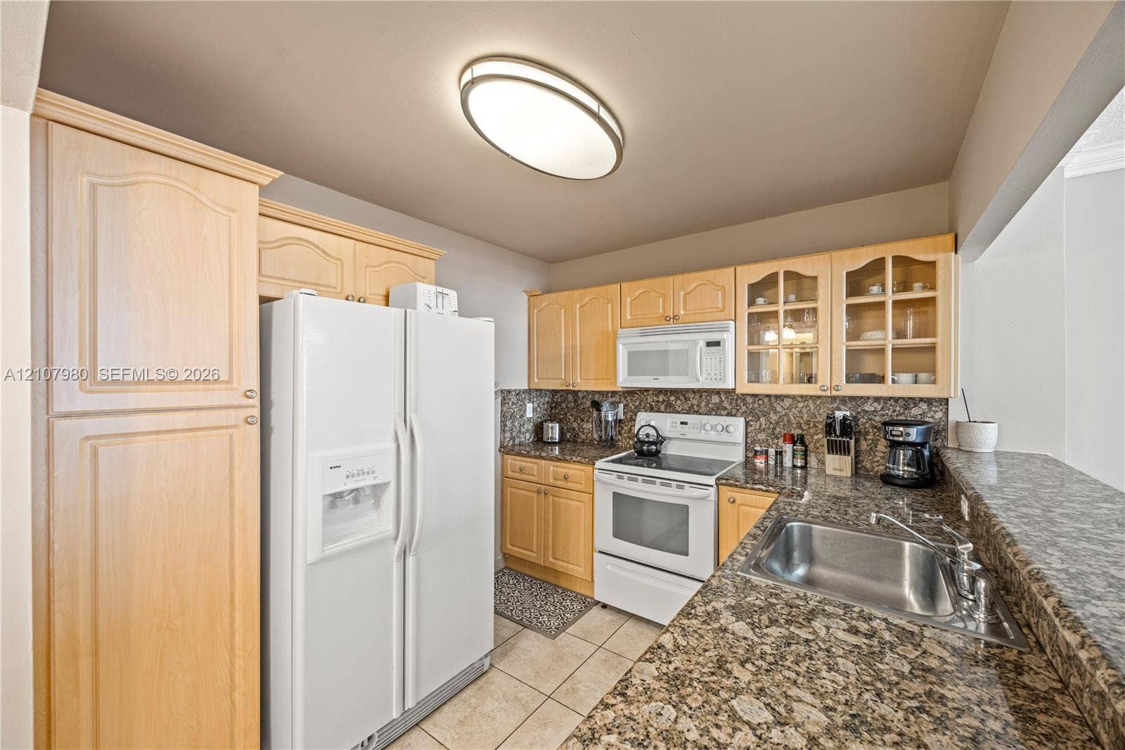 3725 S Ocean Drive, #1120, Hollywood, Hollywood, FL 33019 Kitchen featuring natural-finish wood cabinetry, stone-patterned countertops, a stainless steel undermount sink, glass-paneled upper cabinet doors, and white appliances