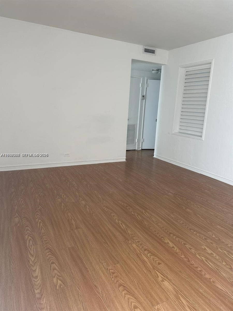Wood-finish flooring, neutral walls, and a window with a fitted shutter