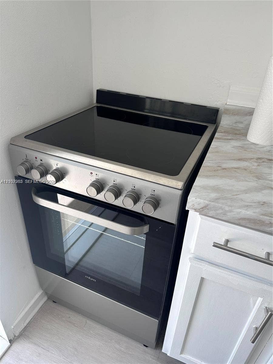 Stainless steel electric range with glass cooktop, paired with white shaker-style cabinetry and neutral stone-finish countertop