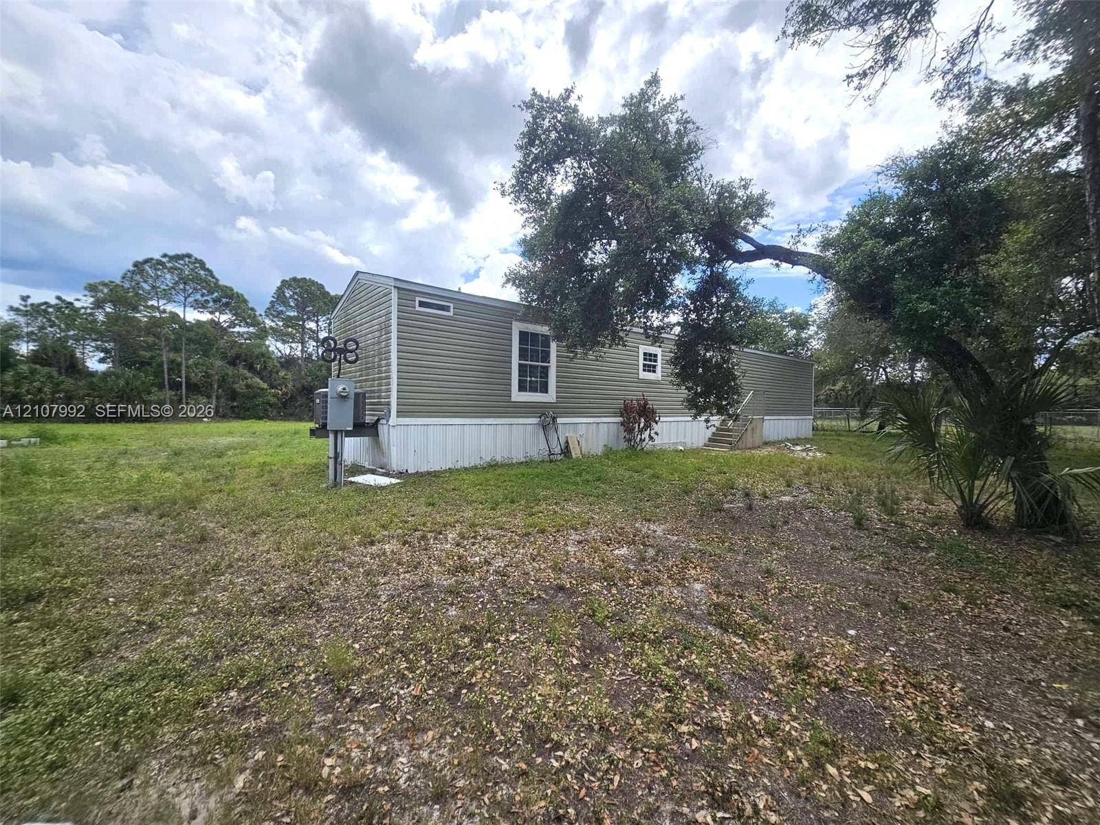 725 S Mayoral Street, Clewiston, FL 33440 Horizontal siding exterior featuring wood-finish steps and mature trees on the surrounding grounds