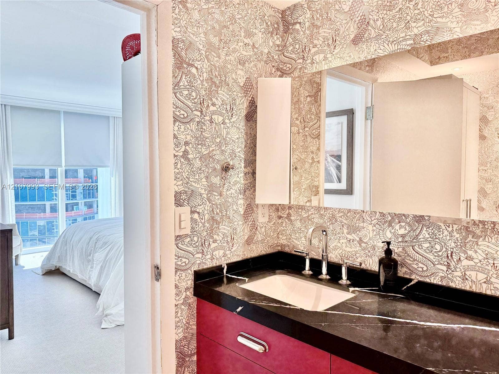 10275 Collins Avenue, #1110, Bal Harbour, Bal Harbour, FL 33154 Bathroom featuring a deep-toned vanity cabinet, integrated dark stone-finish countertop with a rectangular undermount sink, chrome widespread faucet, and large-scale wall mirror set against patterned wallpaper