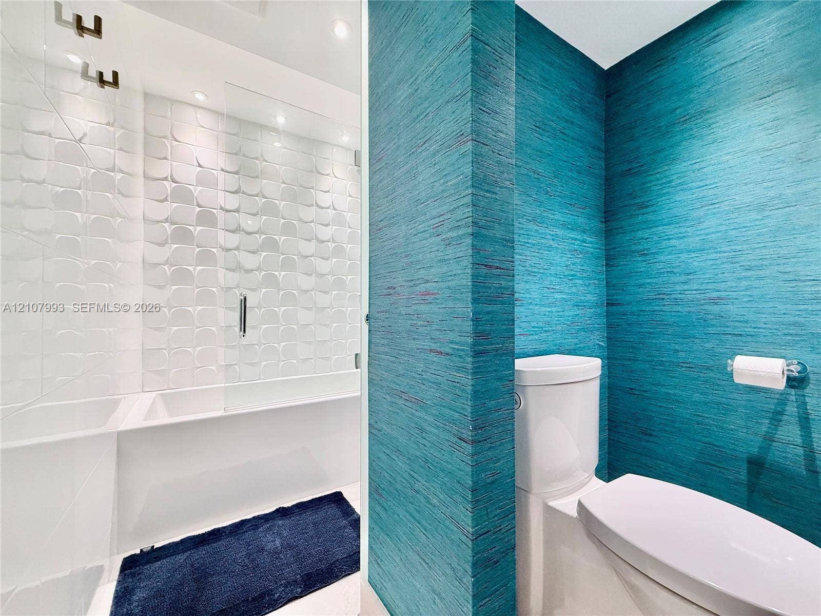 10275 Collins Avenue, #1110, Bal Harbour, Bal Harbour, FL 33154 Textured teal wall covering, geometric white tiled shower surround, glass shower partition, and white dual-flush toilet