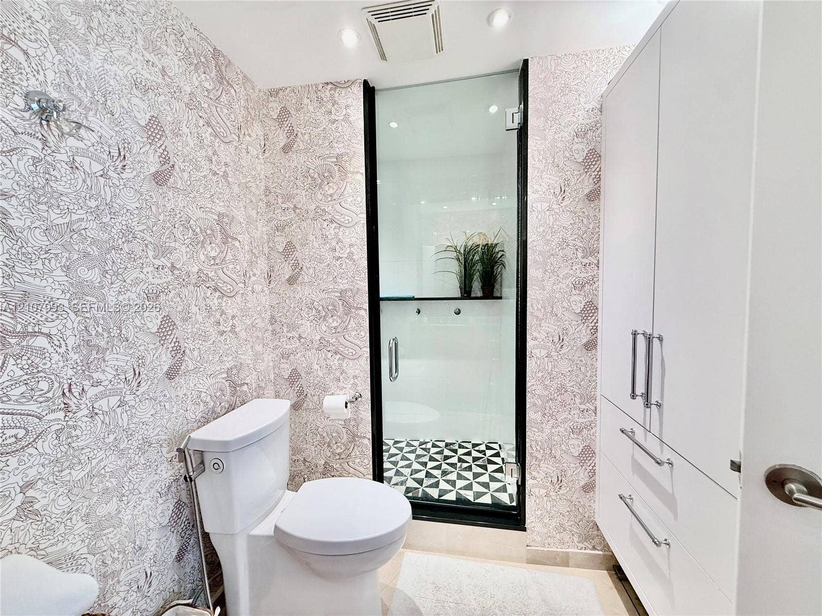 10275 Collins Avenue, #1110, Bal Harbour, Bal Harbour, FL 33154 Bathroom featuring patterned wall coverings, a built-in white cabinetry unit with silver-tone hardware, a glass-enclosed shower with black trim, and geometric patterned flooring