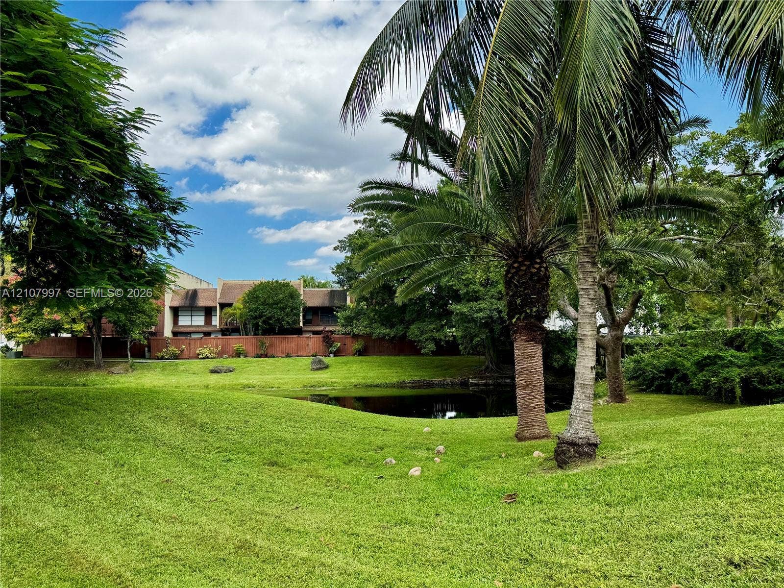 6814 SW 114th Place, #G65, Miami, FL 33173 Expansive grounds featuring a manicured lawn, mature palm trees, and a pond