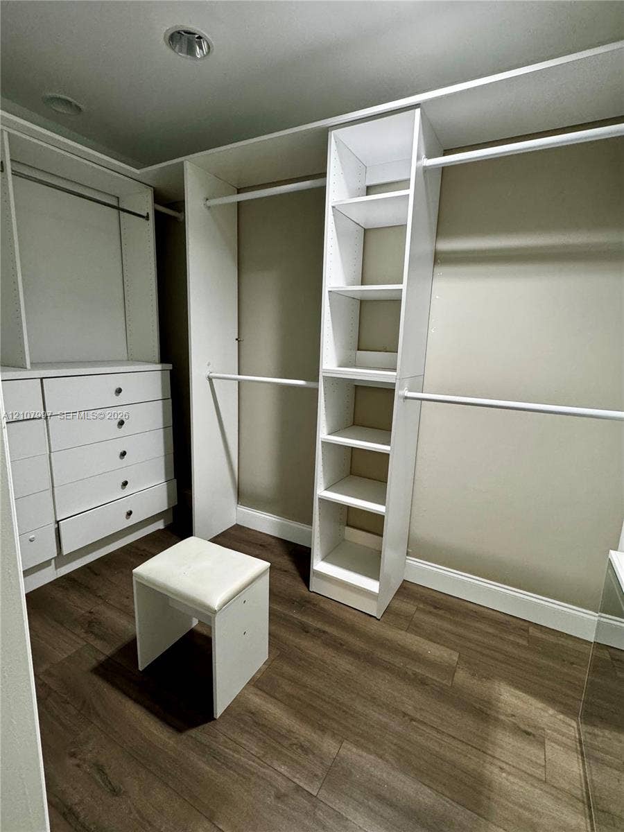 6814 SW 114th Place, #G65, Miami, FL 33173 Walk-in closet featuring white built-in shelving, integrated dresser drawers, hanging rods, and wood-finish flooring
