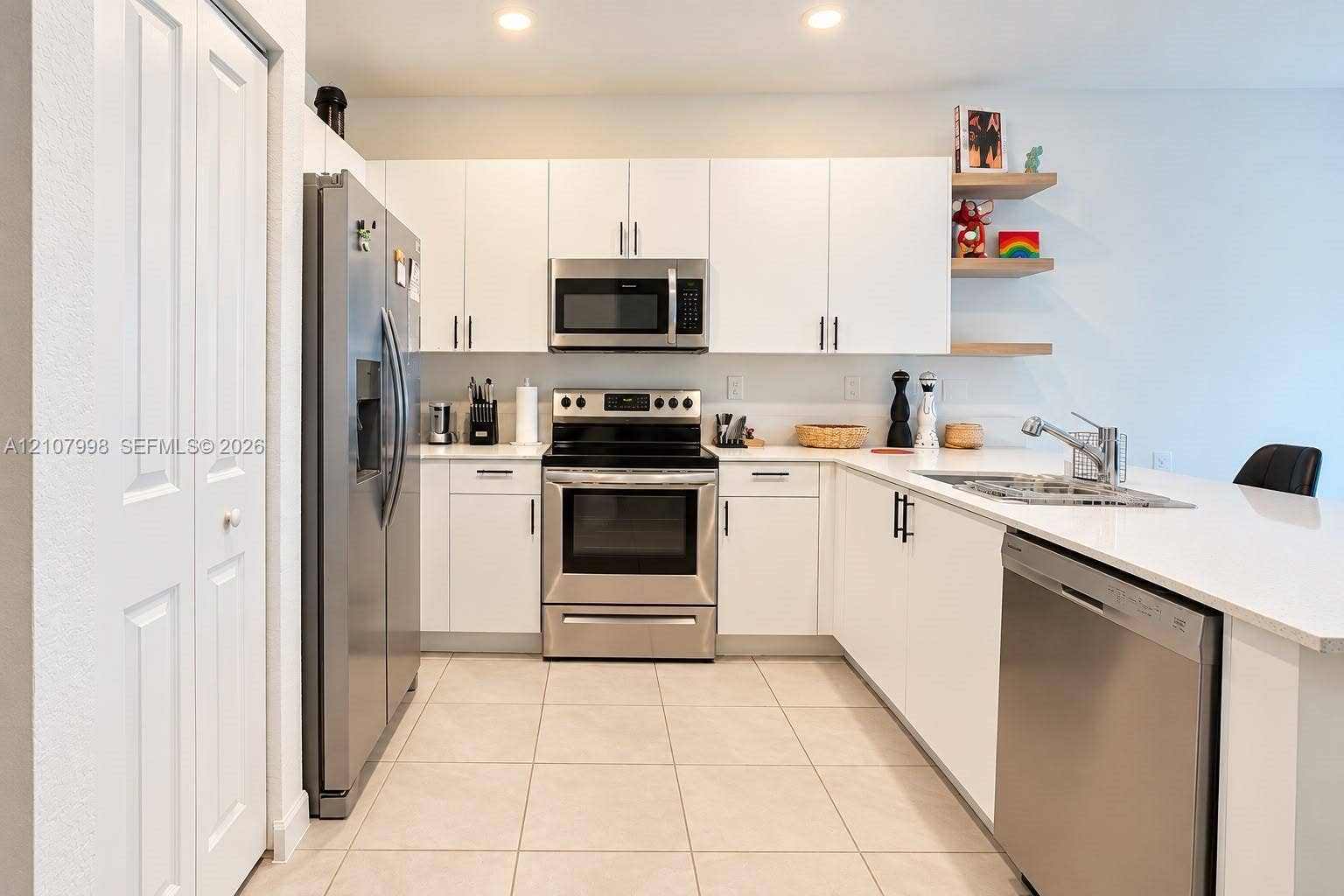 23471 SW 129th Avenue, Homestead, Homestead, FL 33032 Kitchen featuring white flat-panel cabinetry, stainless steel appliances, white solid-surface countertops, tile flooring, and built-in floating wood shelving