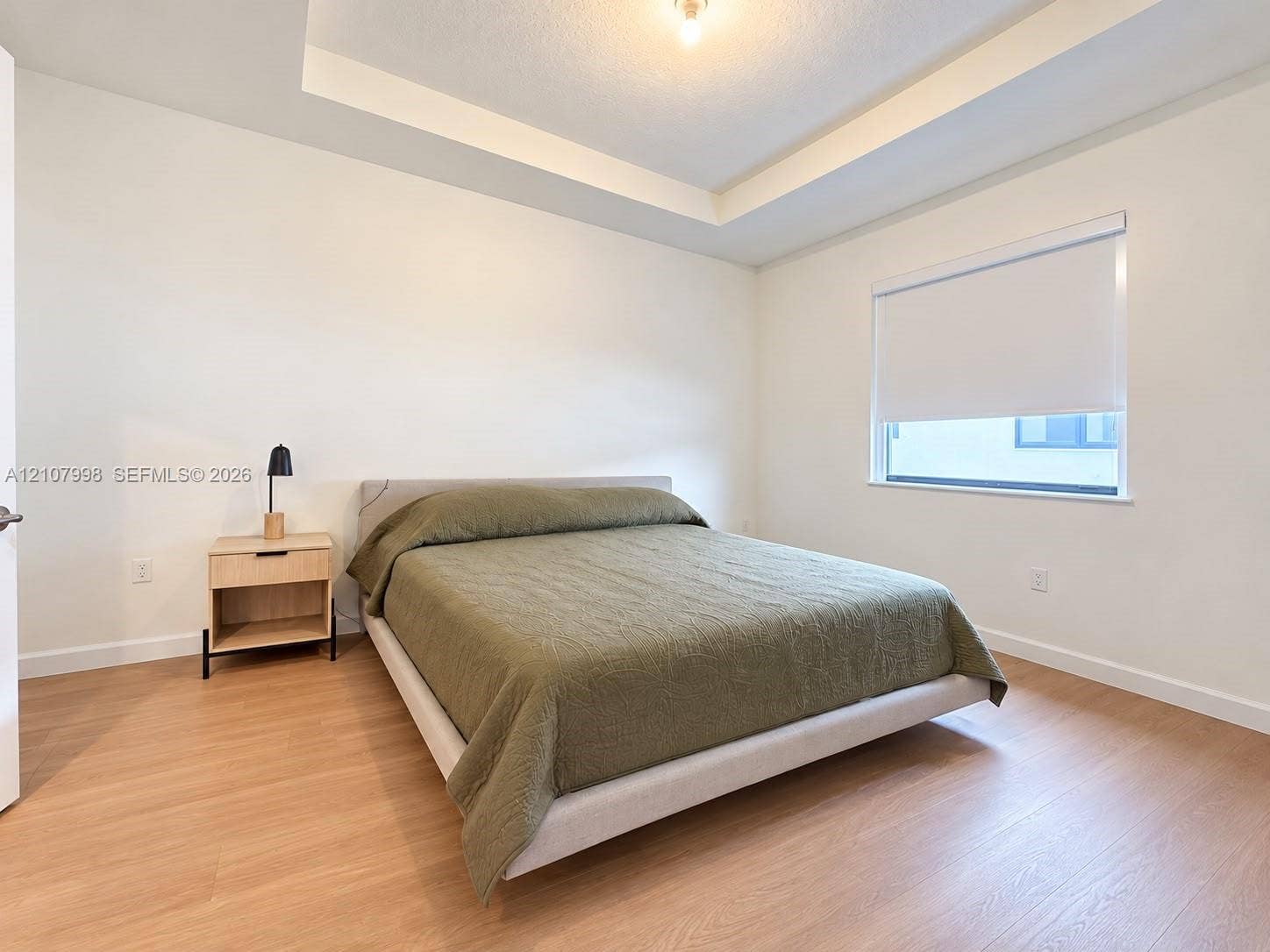 23471 SW 129th Avenue, Homestead, Homestead, FL 33032 Interior space featuring a recessed tray ceiling, light-tone wood-finish flooring, and a window with a retractable roller shade