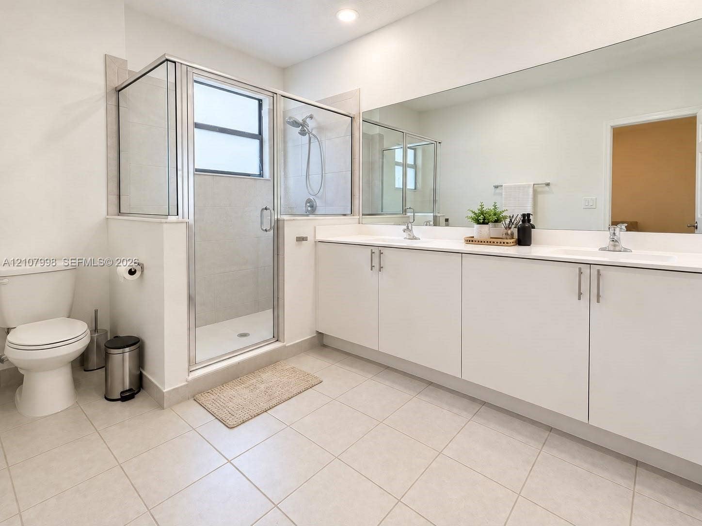 23471 SW 129th Avenue, Homestead, Homestead, FL 33032 Dual-sink vanity with white cabinetry and solid surface countertop, large wall-mounted mirror, glass-enclosed shower with tile surround, and tile flooring