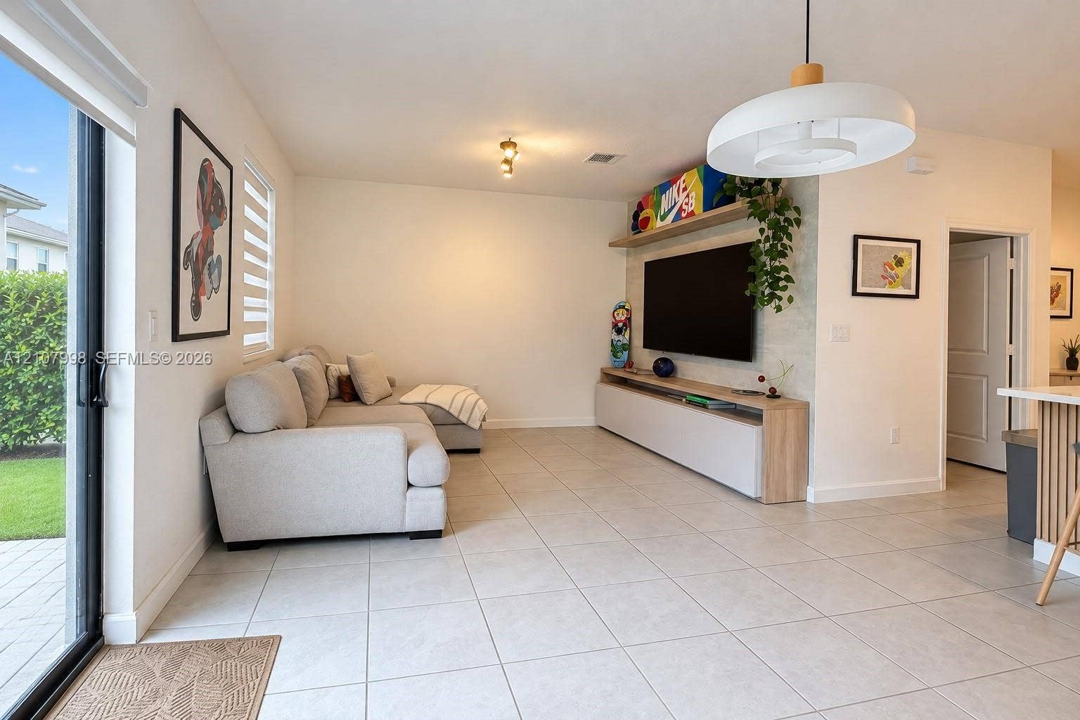 23471 SW 129th Avenue, Homestead, Homestead, FL 33032 Living area featuring large format tile flooring, sliding glass patio doors, built-in media console with light wood finishes, and modern pendant lighting