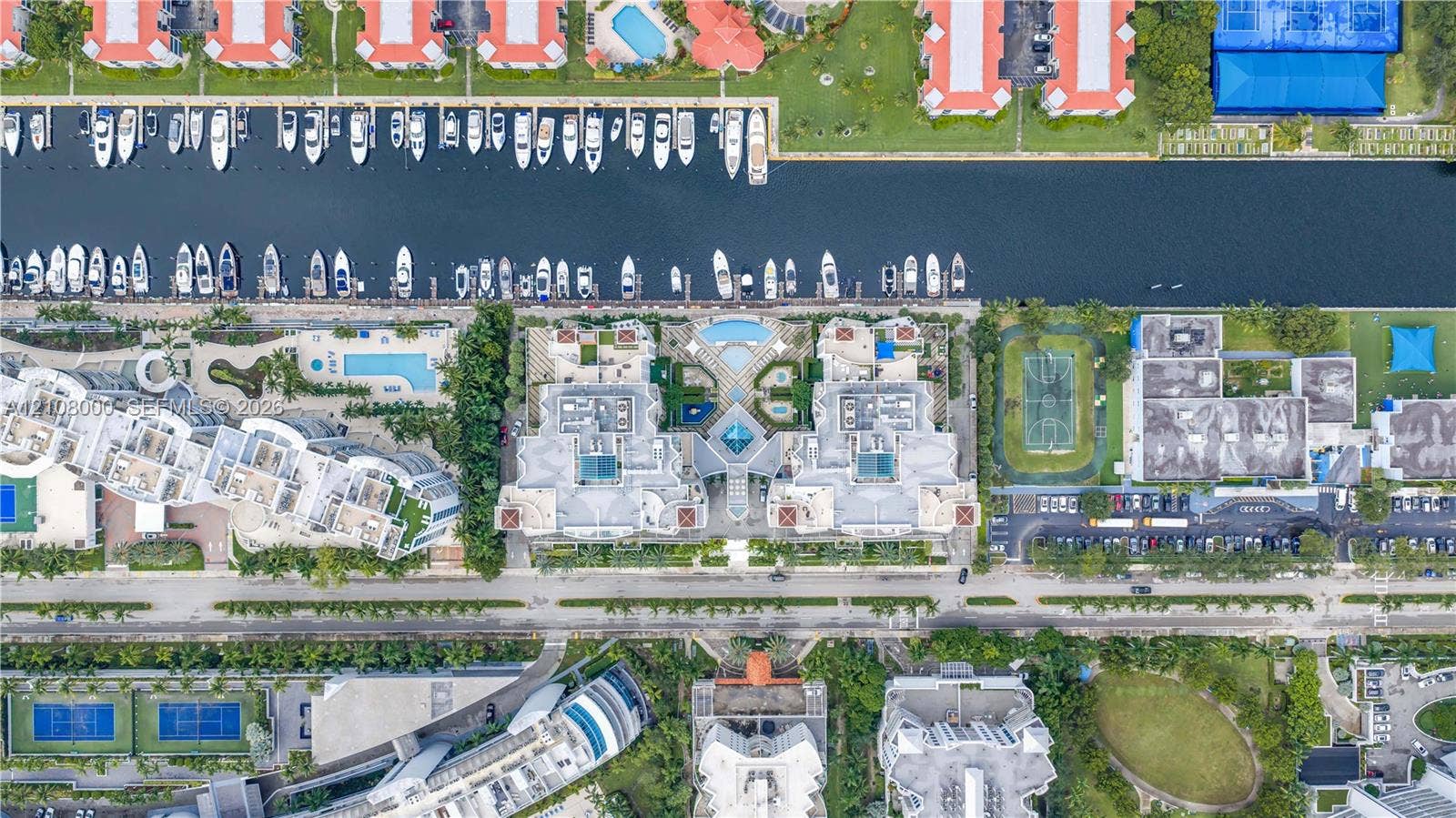 Aventura, FL 33180 Aerial perspective of a waterfront residential complex featuring direct canal access, boat slips, paved parking, swimming pools, and sports courts