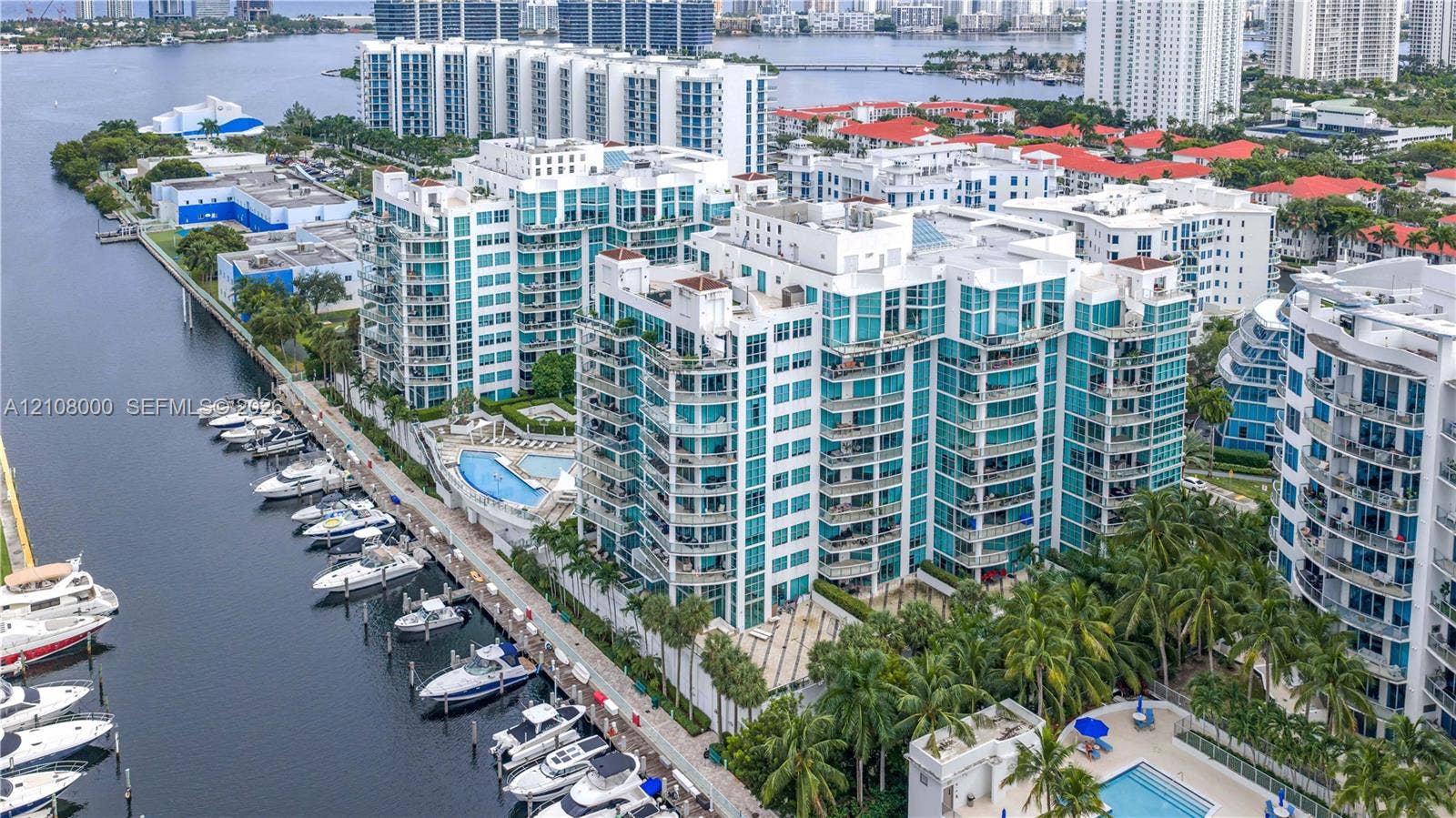 Aventura, FL 33180 High-rise residential building featuring expansive glass paneling, wraparound balconies, deep-water boat slips, and a ground-level swimming pool