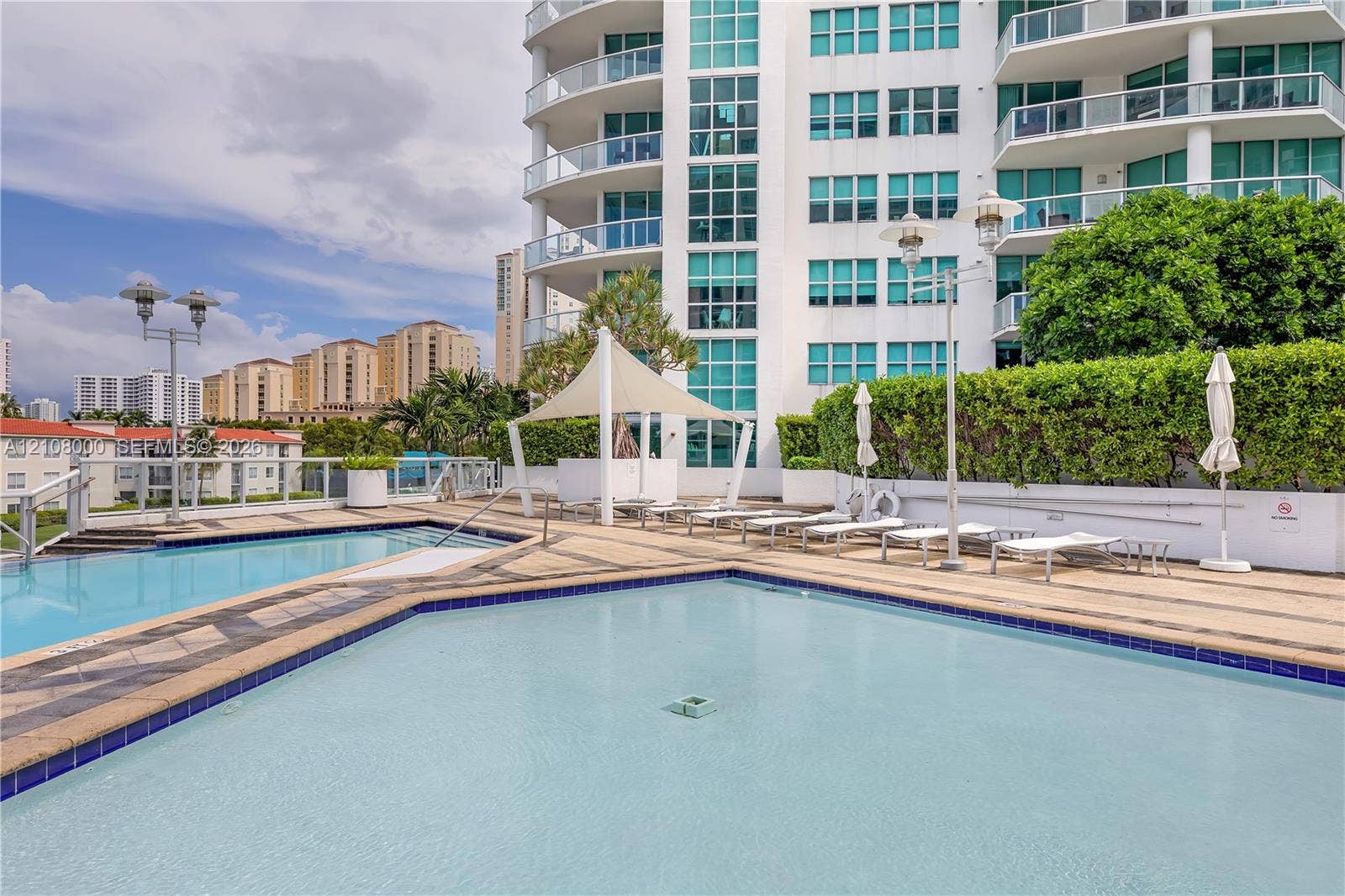 Aventura, FL 33180 Multi-level outdoor pool deck featuring tile surround, shaded seating area with canopy, and perimeter landscaping
