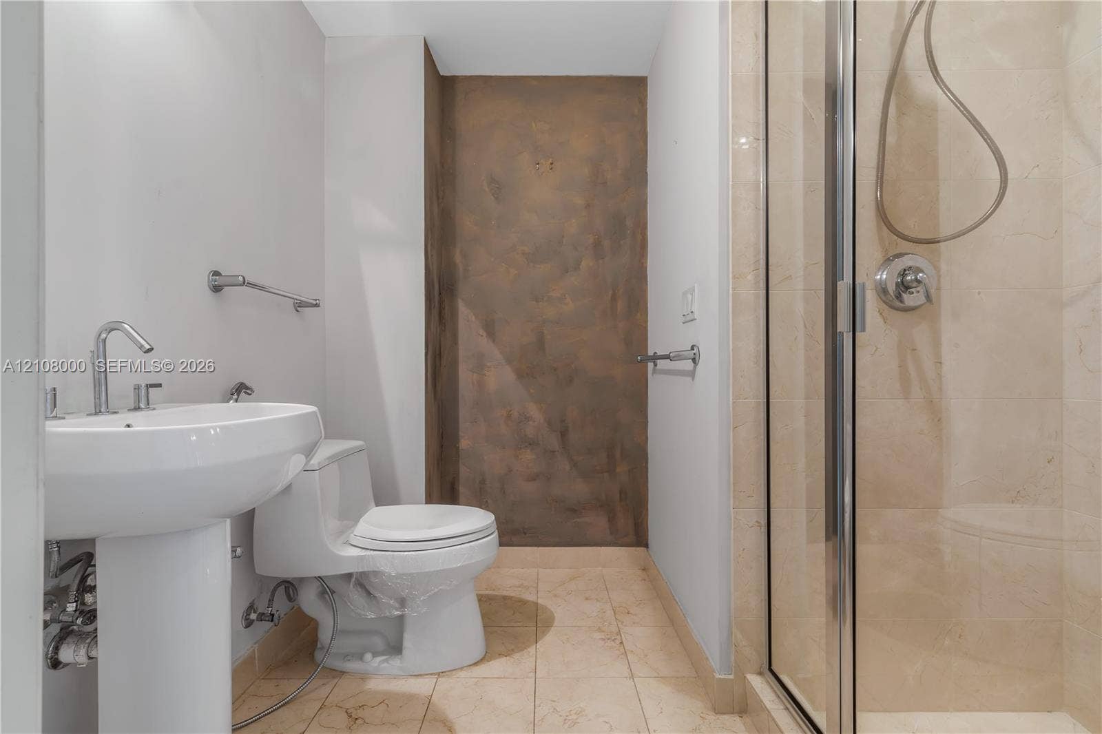 Aventura, FL 33180 Bathroom featuring a pedestal sink, stone-finish floor tiling, glass-enclosed shower with stone-finish wall cladding, and metallic hardware