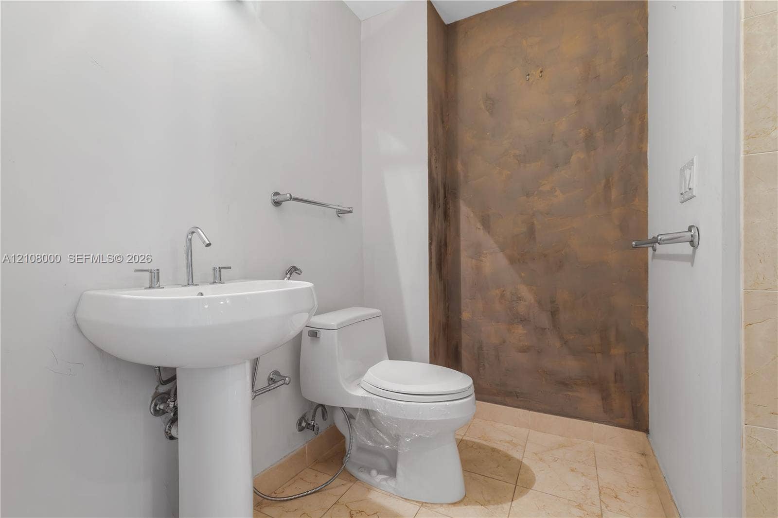 Aventura, FL 33180 White porcelain pedestal sink with polished chrome faucet, dual-flush toilet, stone-finish tile flooring, and metallic-finish accent wall