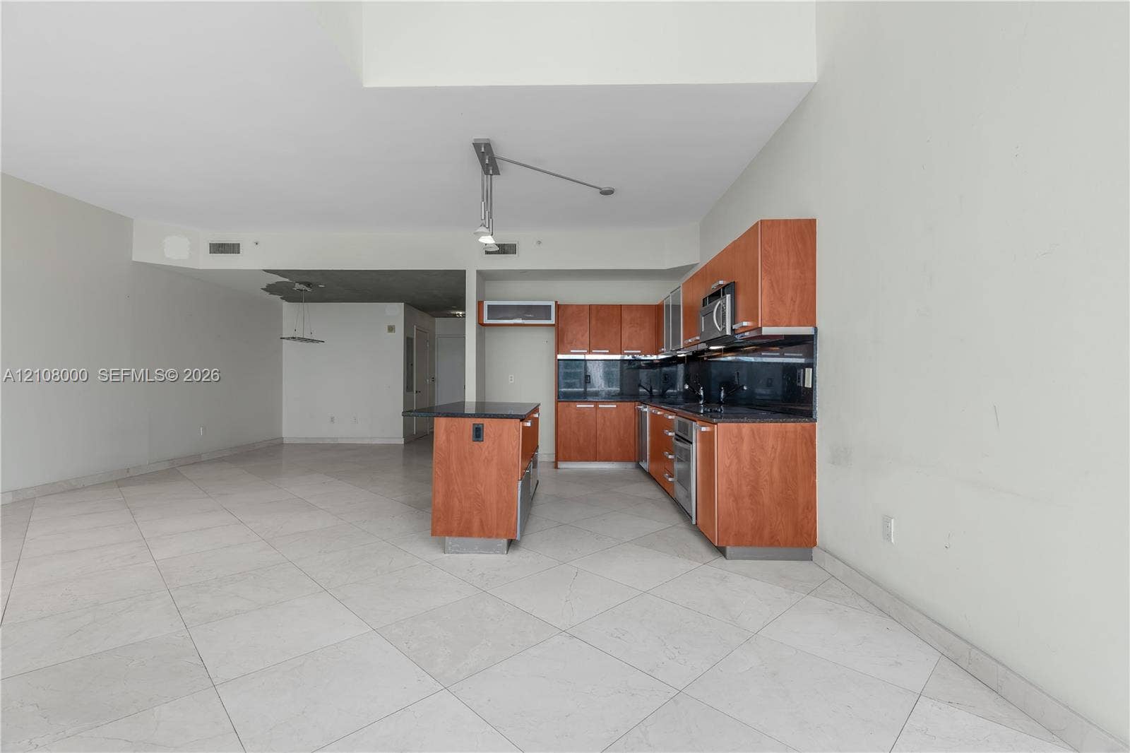 Aventura, FL 33180 Kitchen featuring wood-veneer cabinetry, stone countertops, stainless steel appliances, a central island, and large-format tile flooring