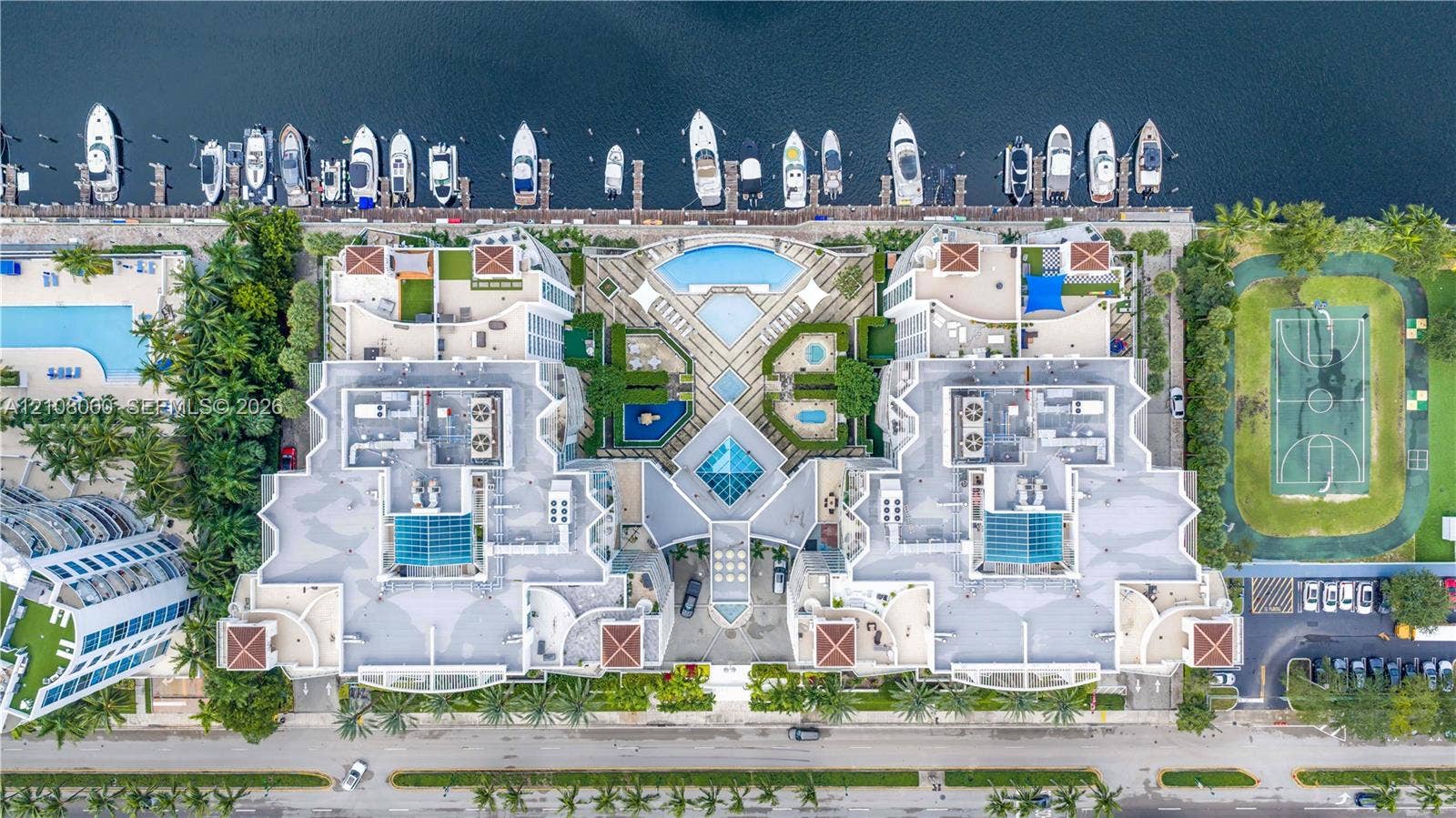 Aventura, FL 33180 Aerial perspective of a multi-structure property featuring deep-water boat slips, multiple swimming pools, a hard-court sports facility, and landscaped grounds