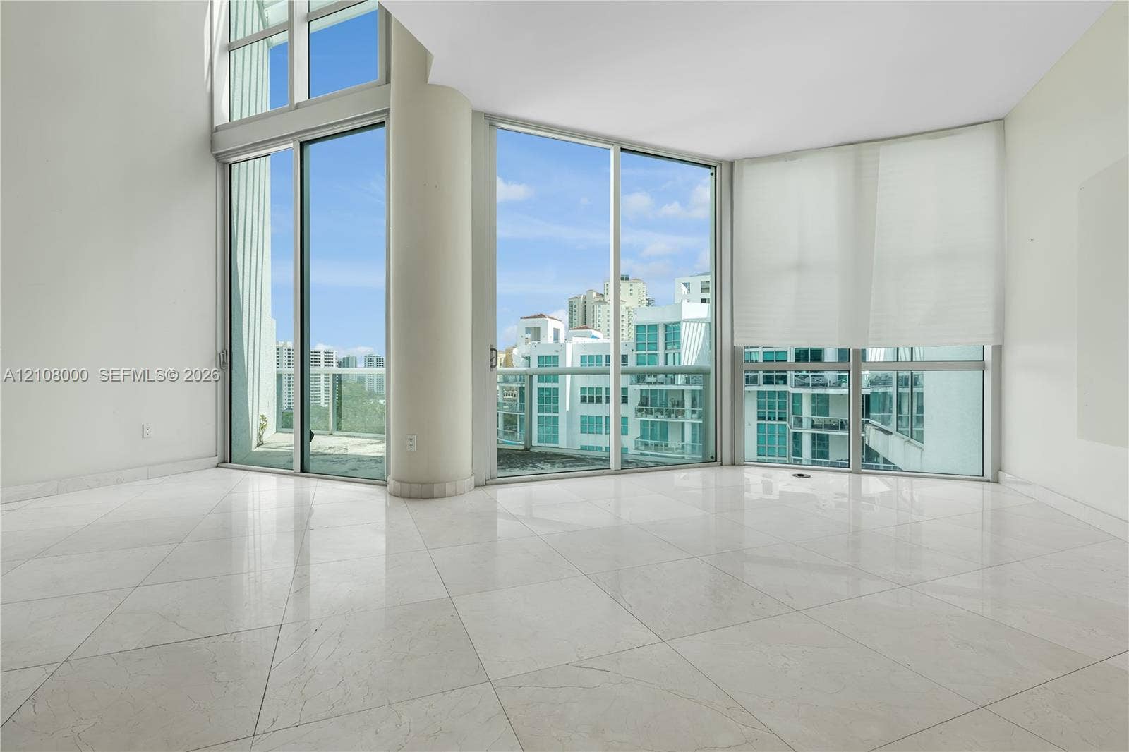 Aventura, FL 33180 Floor-to-ceiling windows, high ceilings, large-format tile flooring, circular structural column, and glass-railing balcony