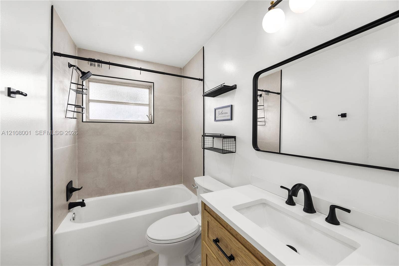 2418 Polk Street, #105, Hollywood, Hollywood, FL 33020 Bathroom featuring wood-finish cabinetry, a white countertop with an integrated basin, a matte black faucet, a tub-shower combination with floor-to-ceiling tile, and a rectangular mirror with a black frame