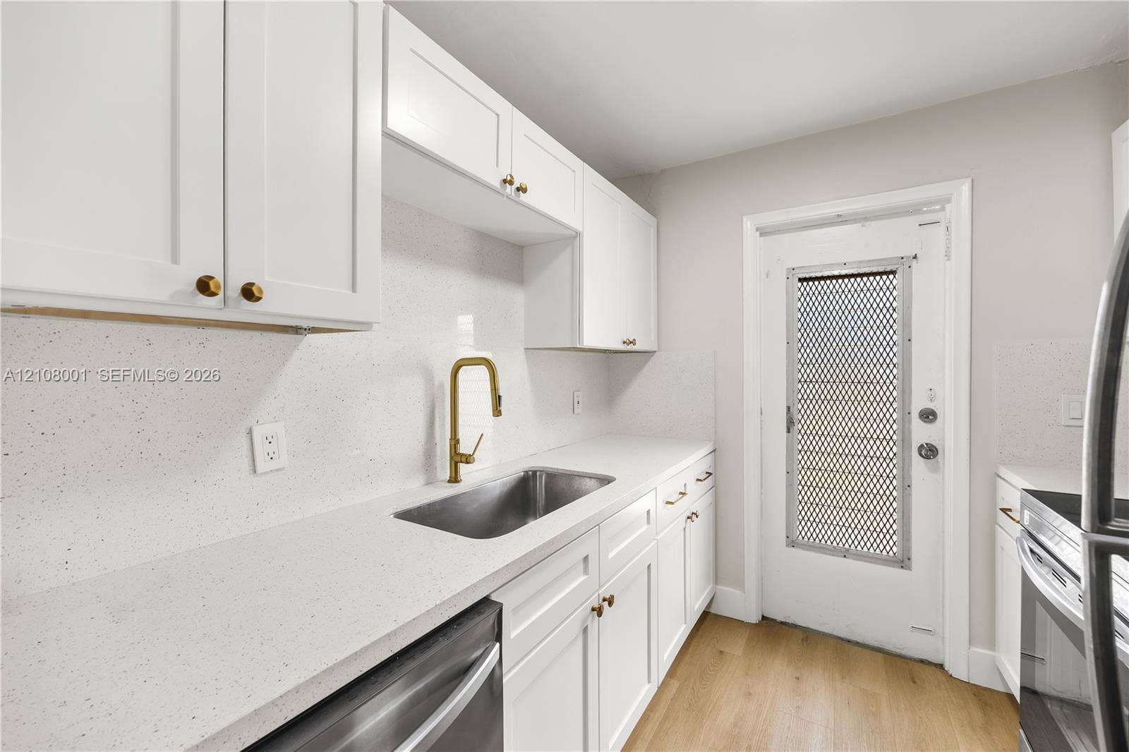 2418 Polk Street, #105, Hollywood, Hollywood, FL 33020 Kitchen featuring white shaker-style cabinetry, solid-surface countertops, a stainless steel undermount sink with a gold-tone gooseneck faucet, and wood-finish flooring