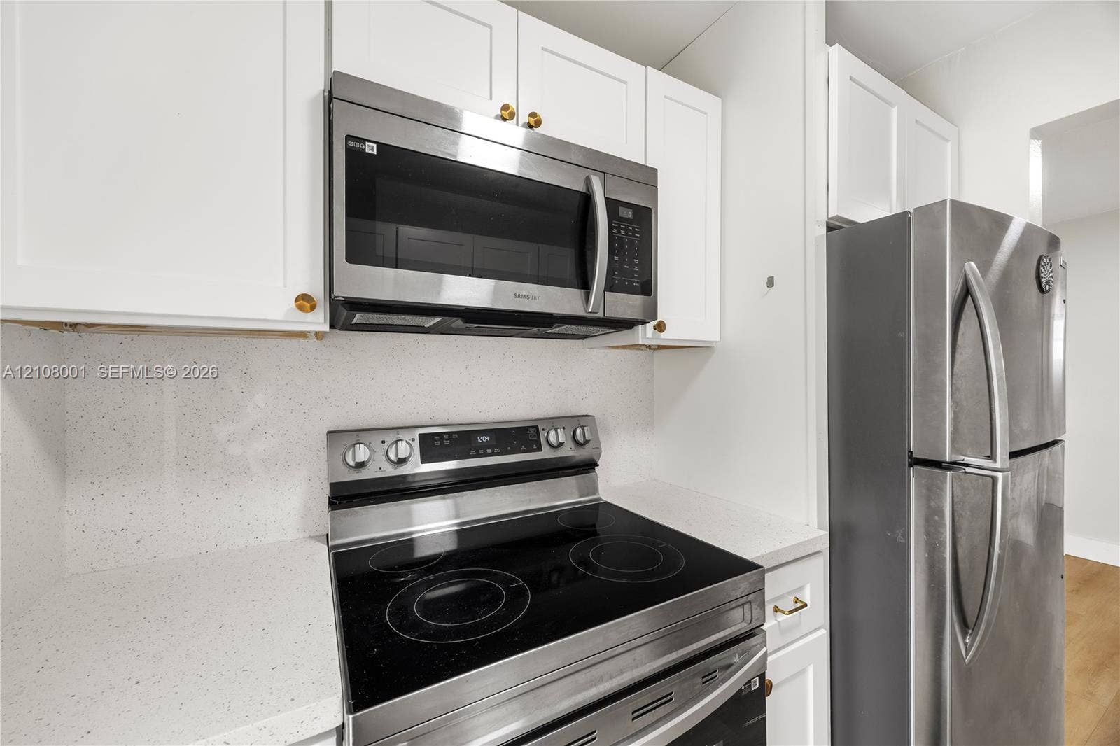 2418 Polk Street, #105, Hollywood, Hollywood, FL 33020 White shaker-style cabinetry, stainless steel microwave, glass-top electric range, stainless steel refrigerator, and solid-surface countertop with matching backsplash