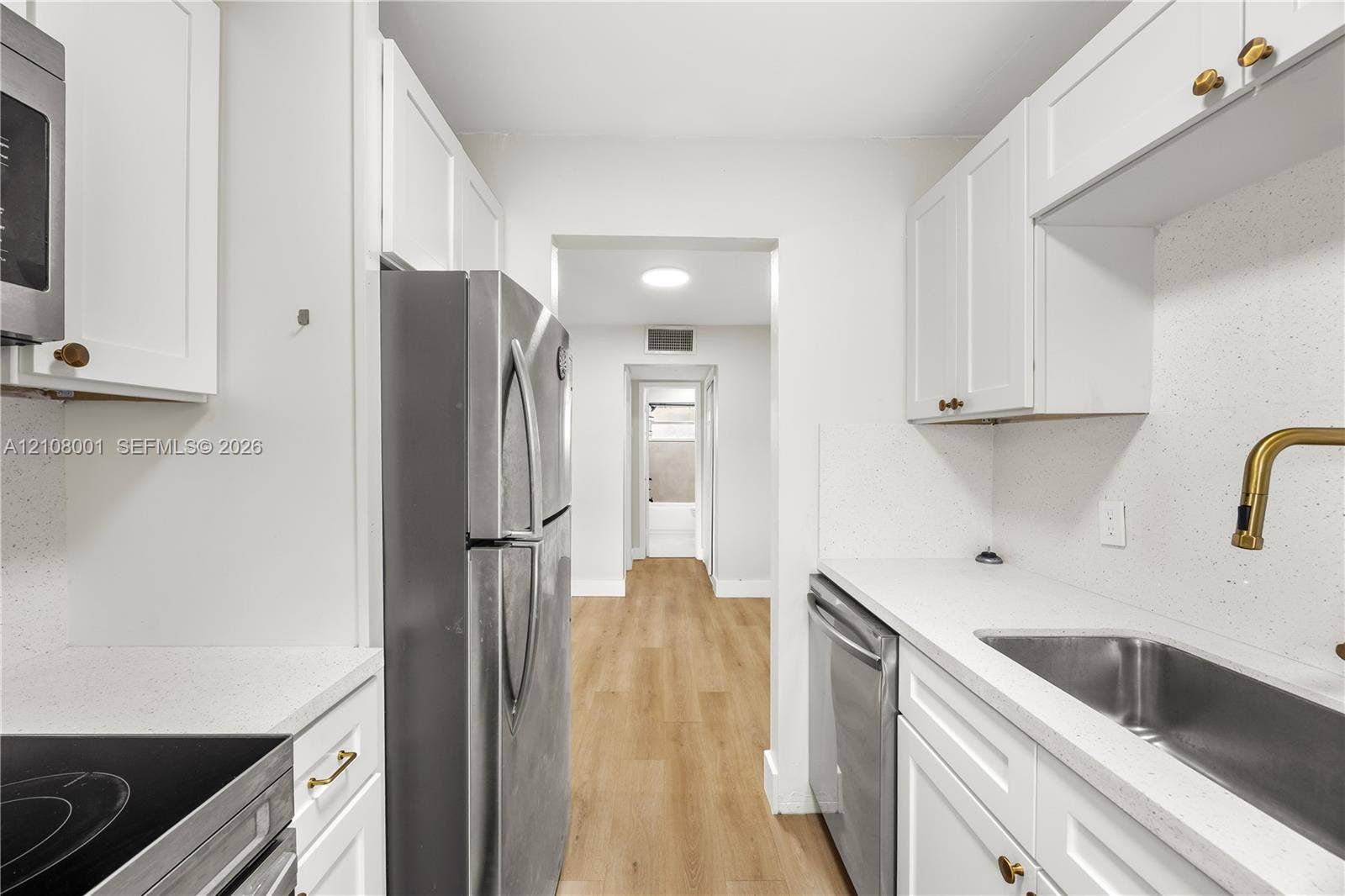 2418 Polk Street, #105, Hollywood, Hollywood, FL 33020 Kitchen featuring white Shaker-style cabinetry, light-toned composite countertops, stainless steel appliances, and wood-finish flooring