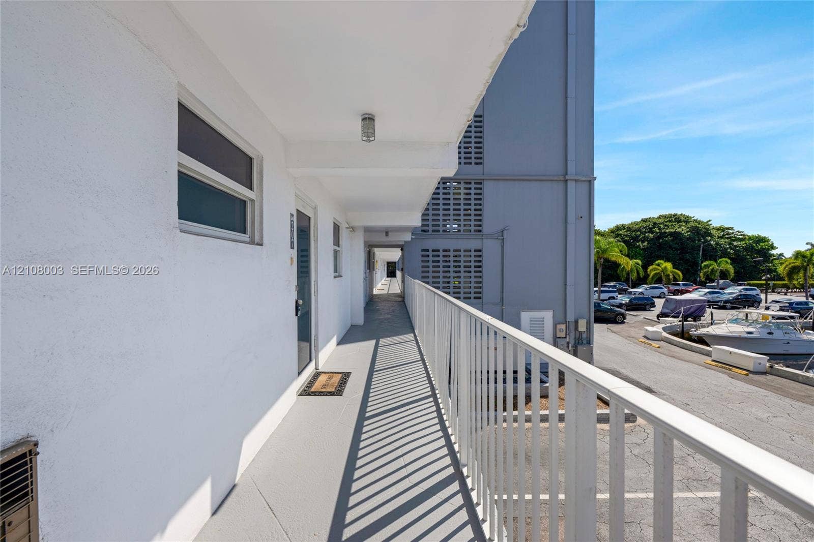 1536 SE 15th Court, #207, Deerfield Beach, FL 33441 Exterior walkway featuring white stucco walls, painted concrete flooring, and a white metal railing overlooking a paved parking area and marina
