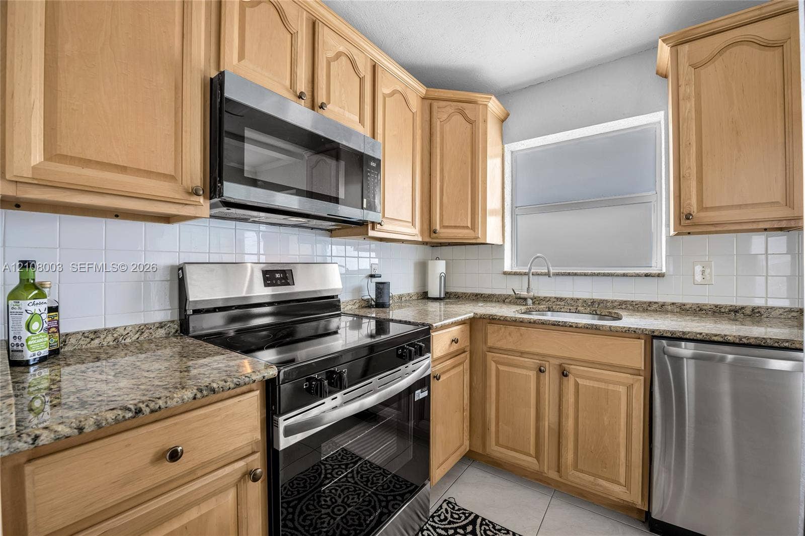 1536 SE 15th Court, #207, Deerfield Beach, FL 33441 Kitchen featuring natural wood cabinetry, stone-finish countertops, stainless steel appliances, a white tile backsplash, and a metal faucet with an integrated sink