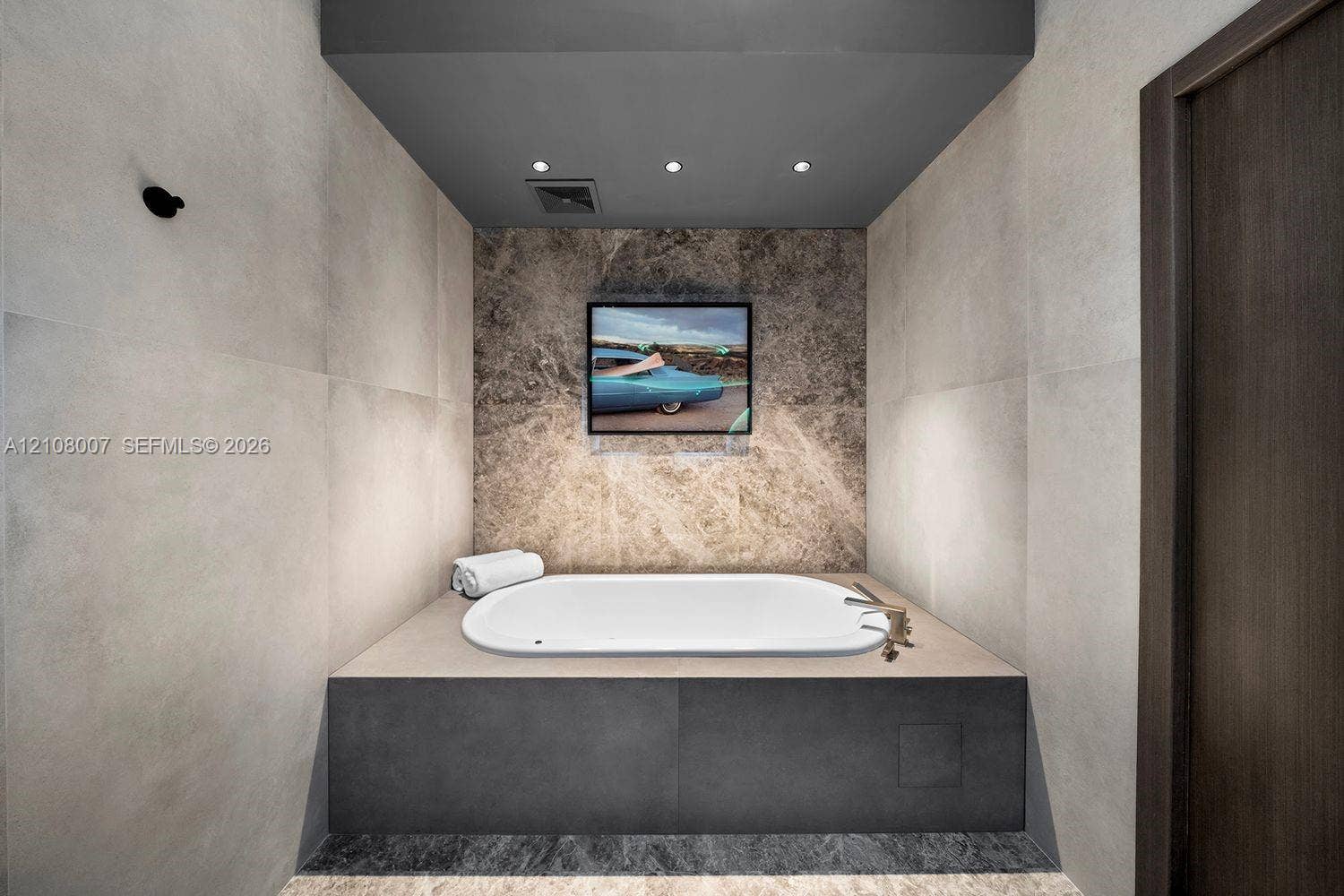 Built-in drop-in bathtub featuring a dark stone-finish base, large-format matte wall tiles, natural stone accent wall, and recessed ceiling lighting