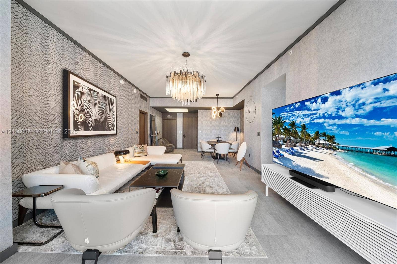 Textured wall coverings, crystal-accented chandelier, wood-finish flooring, custom-slatted built-in media console, and recessed ceiling lighting