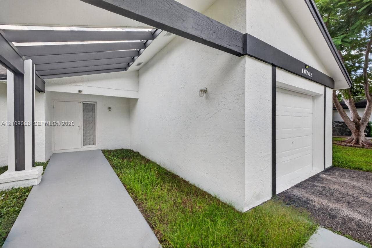 16708 SW 5th Way, Weston, Weston, FL 33326 Stucco exterior featuring a covered pergola entryway, painted wood-beam detailing, a paneled garage door, and a concrete walkway