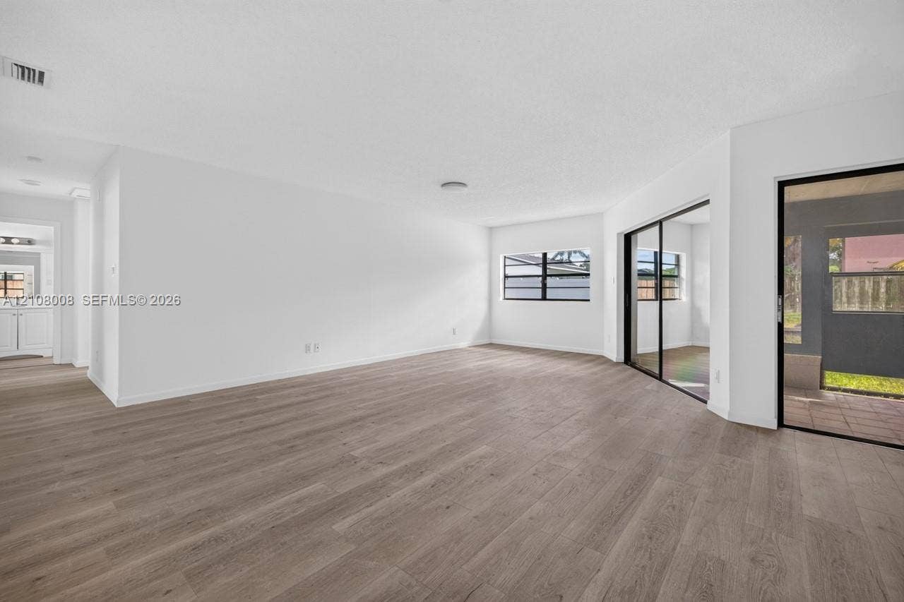 16708 SW 5th Way, Weston, Weston, FL 33326 Open-concept area featuring wood-finish flooring, white walls, black-framed windows, and sliding glass doors with access to an exterior screened enclosure