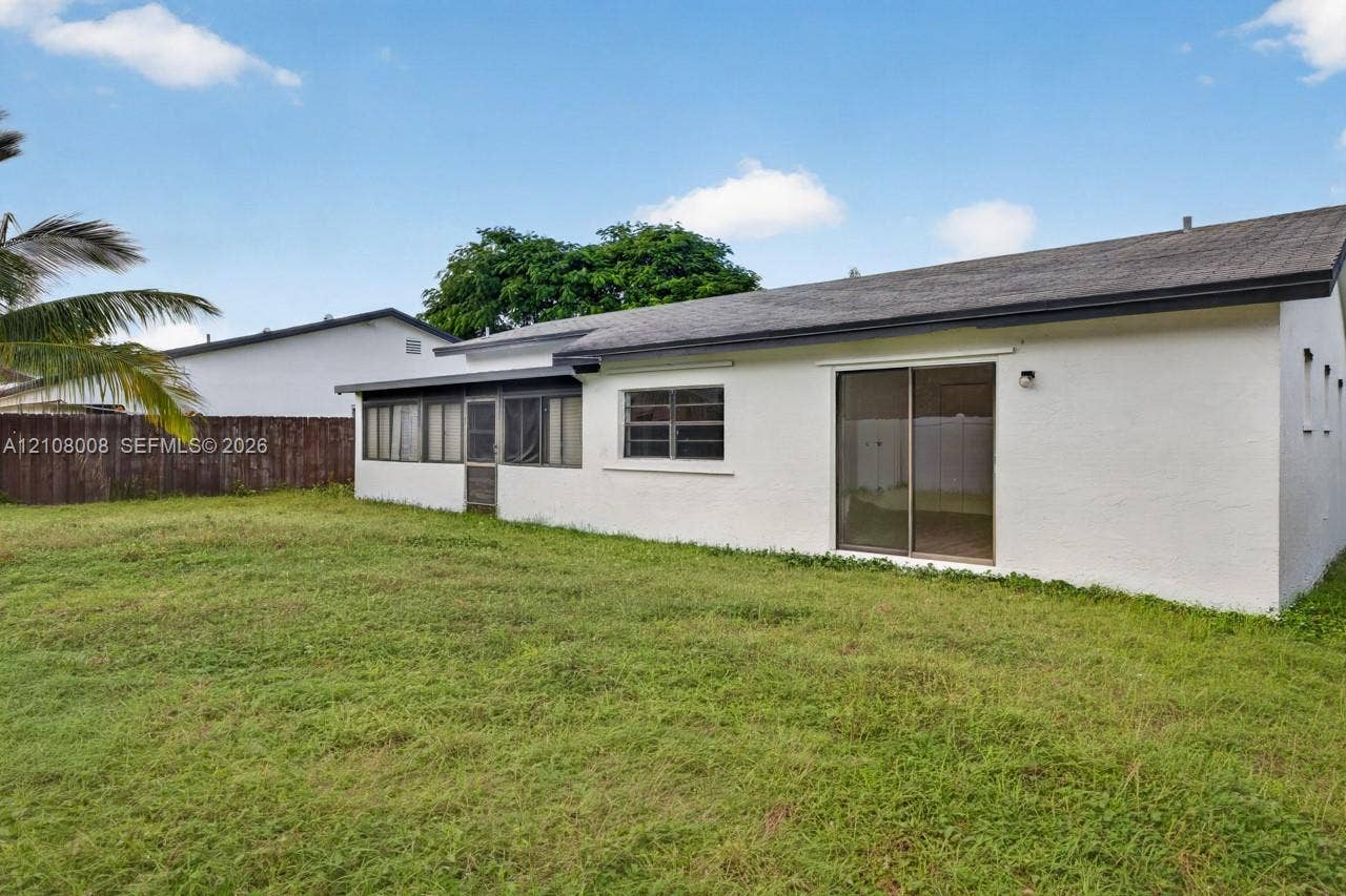 16708 SW 5th Way, Weston, Weston, FL 33326 Exterior view of a residence featuring a white stucco facade, a dark-toned shingle roof, a glass sliding door, and a screened-in lanai, set against a fenced perimeter
