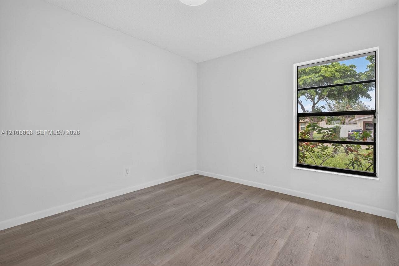 16708 SW 5th Way, Weston, Weston, FL 33326 Neutral-toned interior space featuring wood-finish flooring, white walls, and a multi-pane horizontal window
