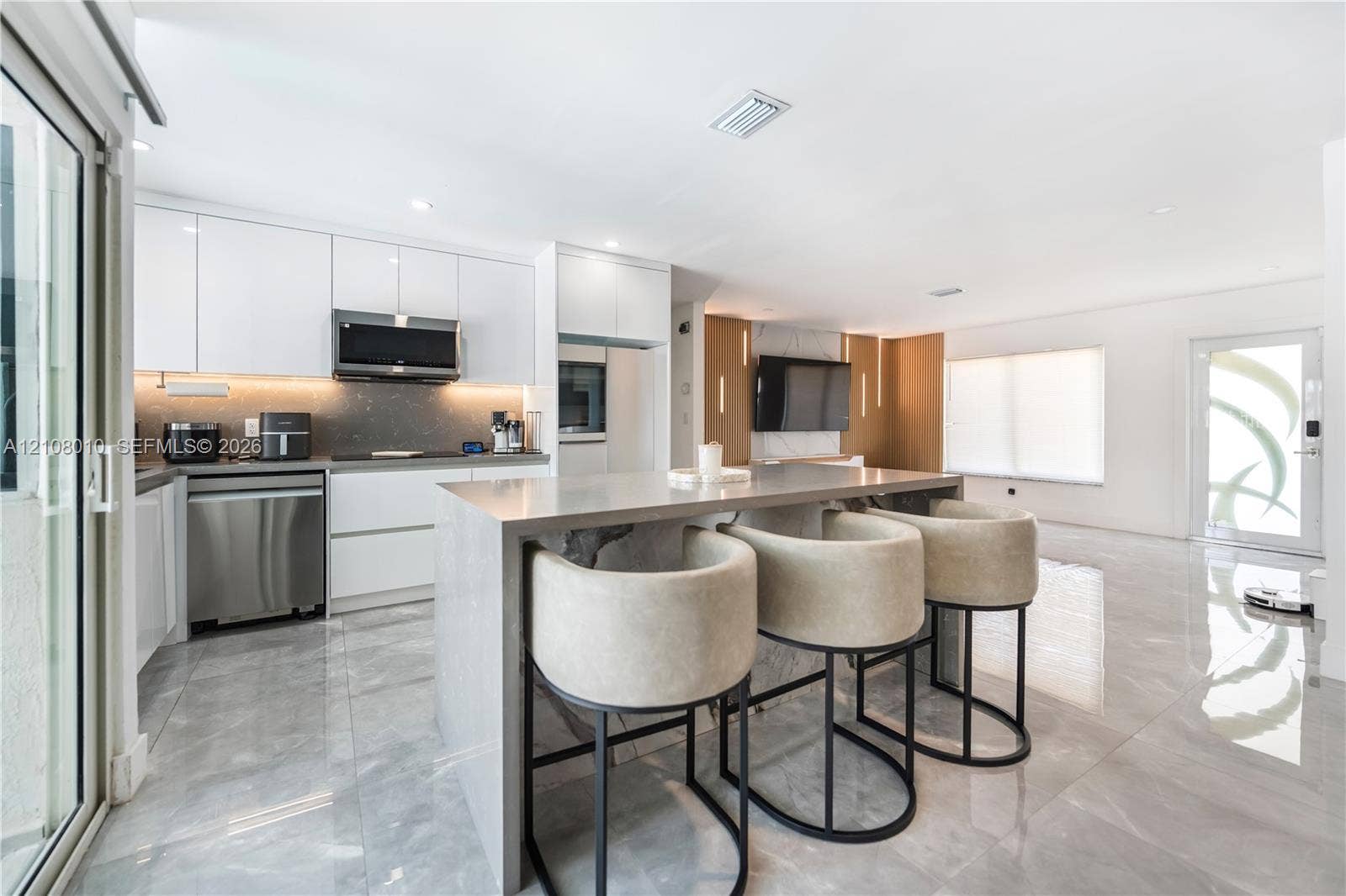 Kitchen featuring high-gloss cabinetry, a waterfall-edge island, polished stone-finish flooring, stainless steel appliances, and integrated under-cabinet lighting