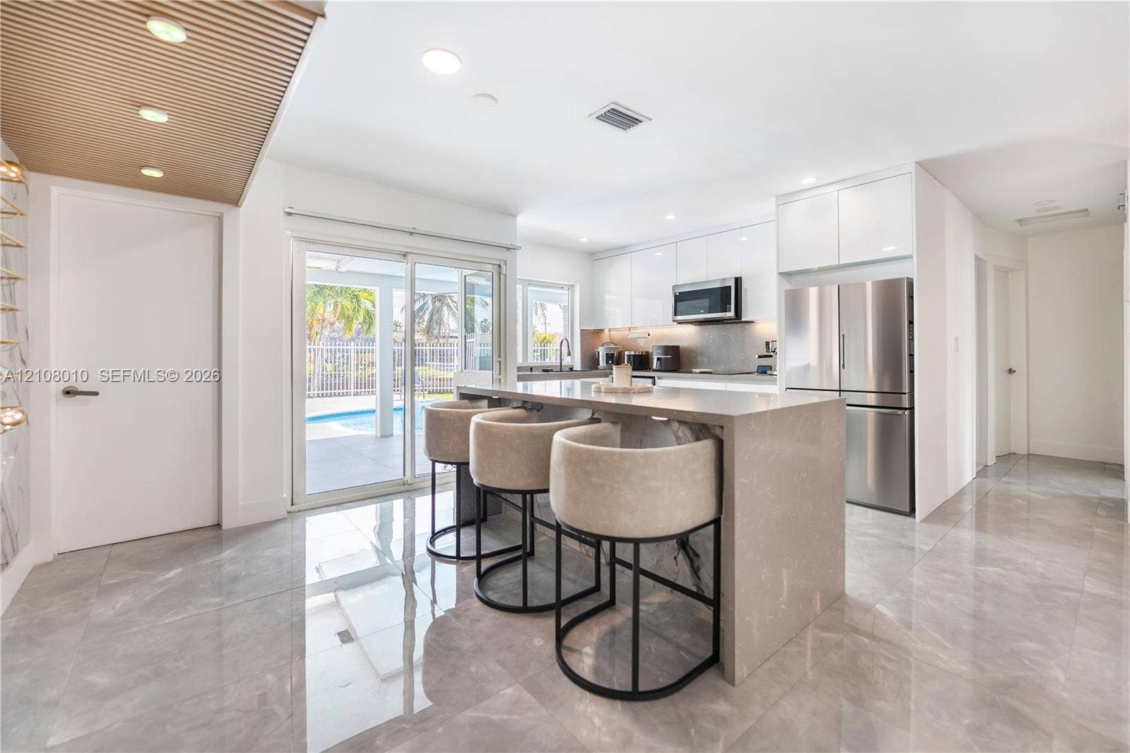 Kitchen featuring high-gloss cabinetry, stone-finish countertops, waterfall-edge island, stainless steel appliances, and large-format tile flooring