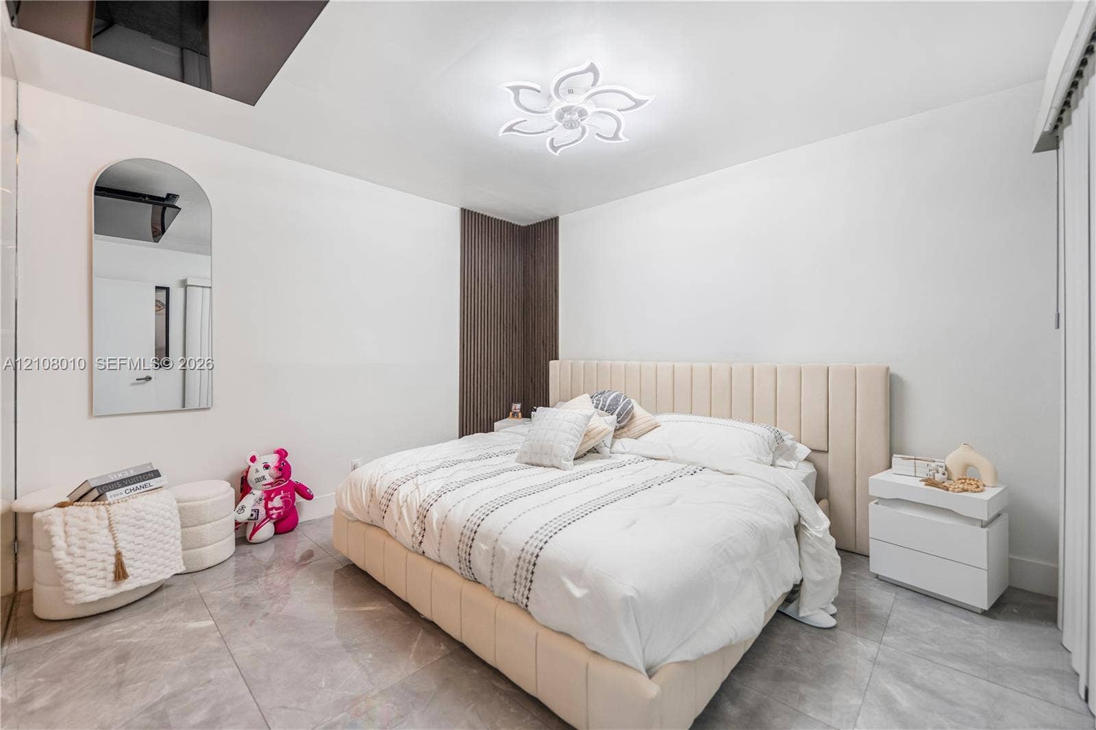 Large-format tile flooring, arched wall mirror, decorative floral-inspired ceiling lighting, and vertical wood-finish accent paneling