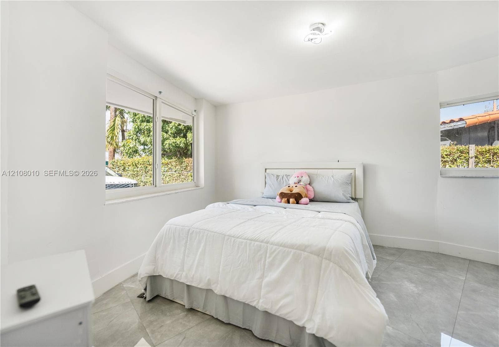 Neutral-toned interior space featuring large-format ceramic tile flooring, bright white wall finishes, sliding windows, and a flush-mount ceiling light fixture