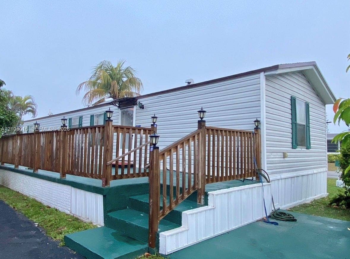 Exterior featuring horizontal light-toned siding, a full-length elevated wooden deck with integrated lighting, and a painted concrete staircase