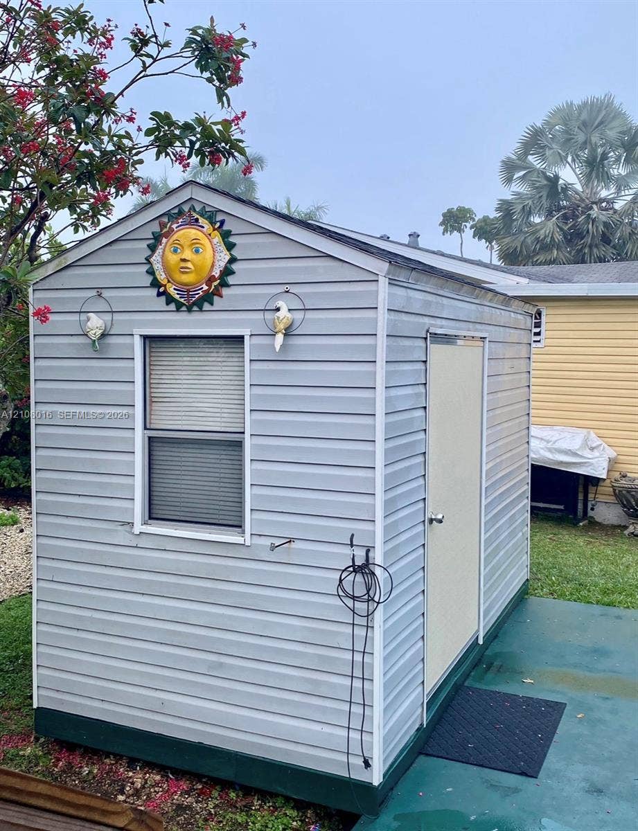 Detached outdoor storage structure featuring grey vinyl siding, a single-entry door, and a multi-pane window
