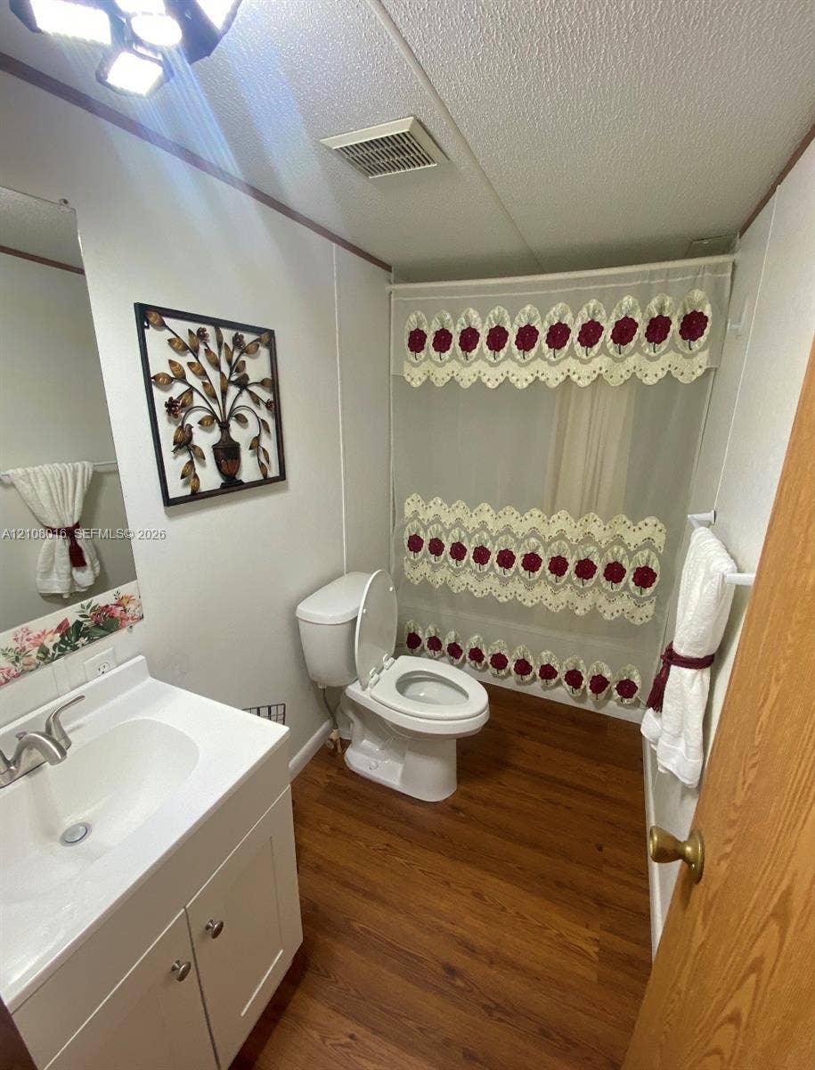 Bathroom featuring a white vanity cabinet with an integrated basin, wood-finish flooring, a combination tub and shower, and a mounted overhead light fixture