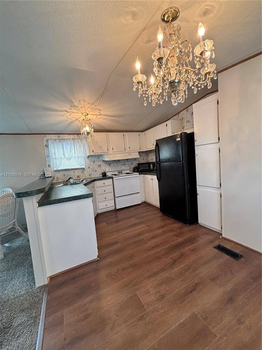Kitchen featuring wood-finish flooring, white cabinetry, a breakfast bar with stone-finish countertops, and an ornate crystal chandelier