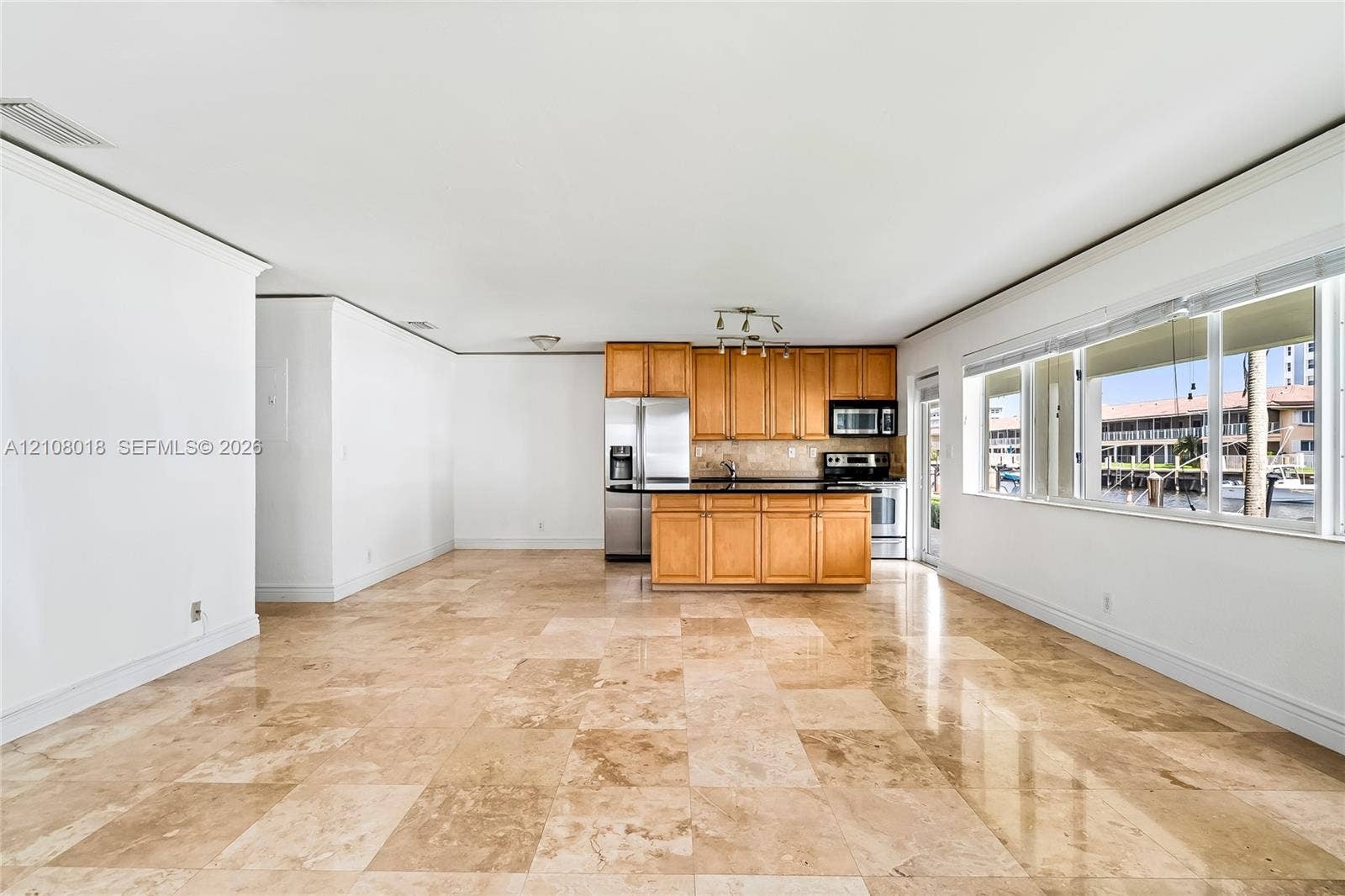 Kitchen featuring light-finish cabinetry, dark solid-surface countertops, and stainless steel appliances, accented by large-format stone tile flooring and panoramic windows