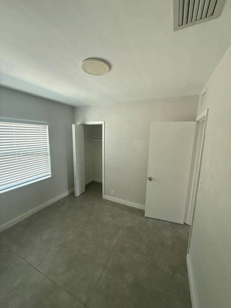 Room featuring large-format ceramic tile flooring, neutral wall paint, and a window with horizontal blinds