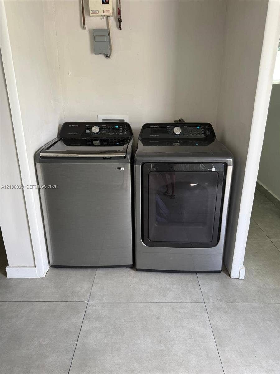 Dedicated laundry alcove featuring large-format ceramic tile flooring and charcoal-finished top-load washing machine and front-load dryer
