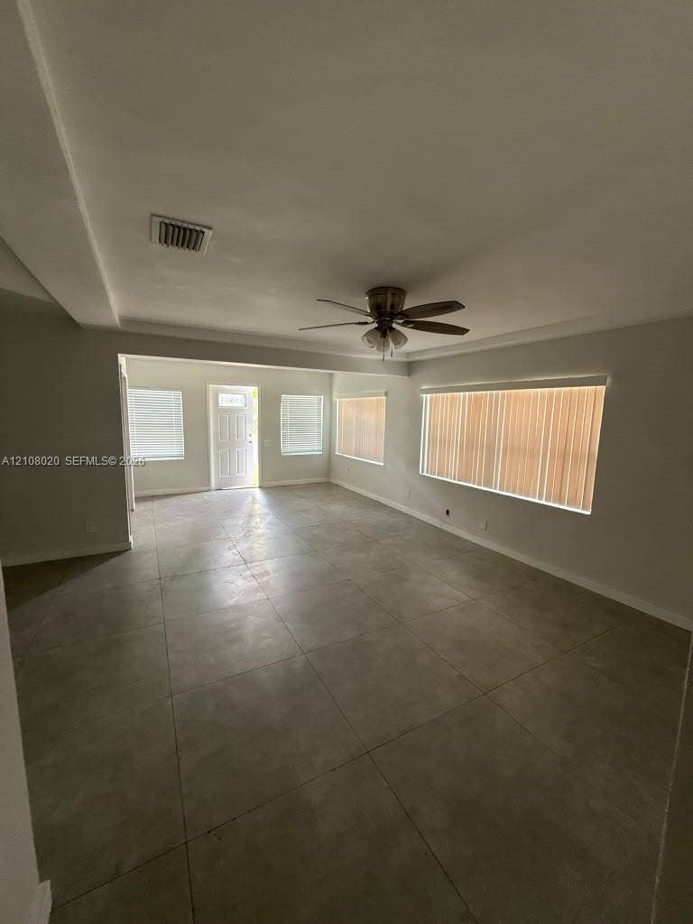 Neutral-toned tile flooring, recessed ceiling design, ceiling fan with integrated lighting, and multiple windows with vertical blinds