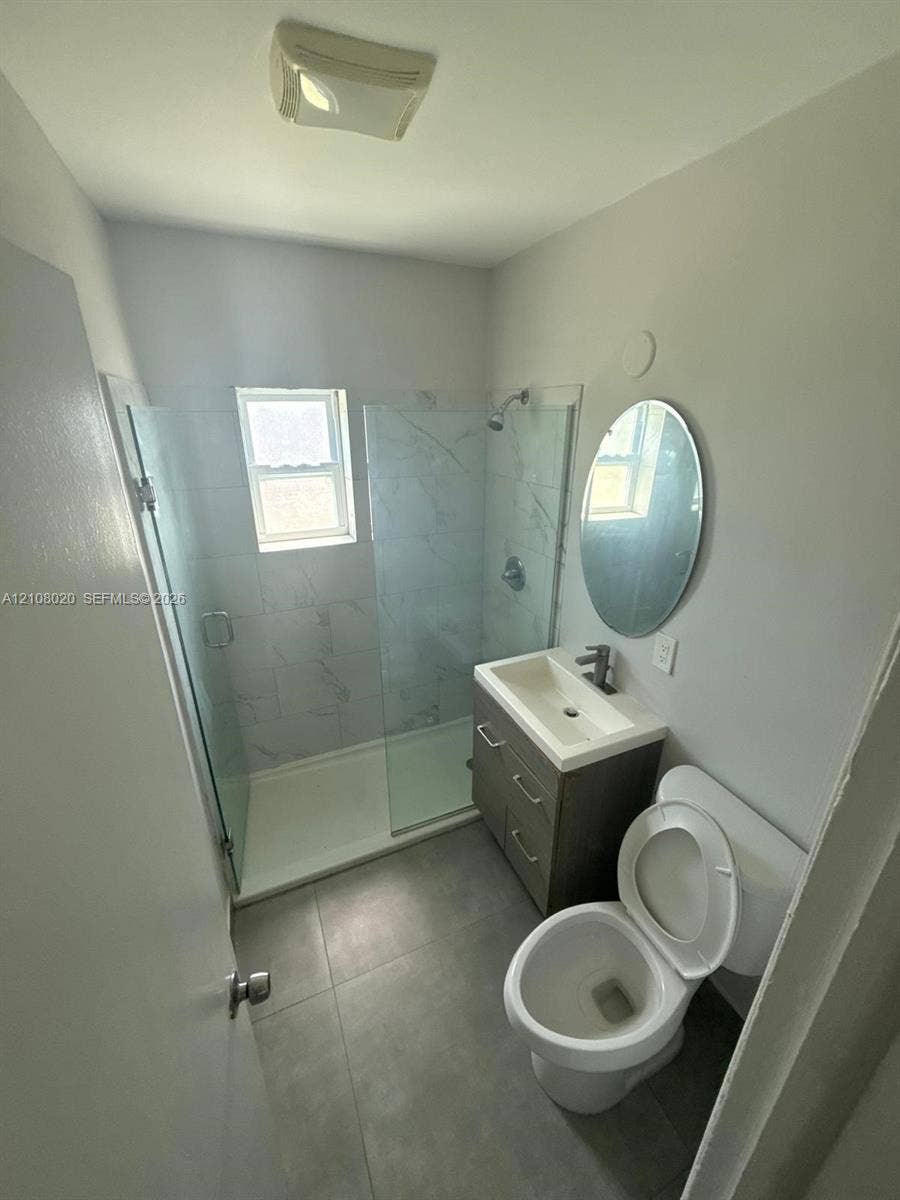 Walk-in shower with floor-to-ceiling tile surround and frameless glass door, vanity with integrated basin and metallic faucet, and oval wall-mounted mirror